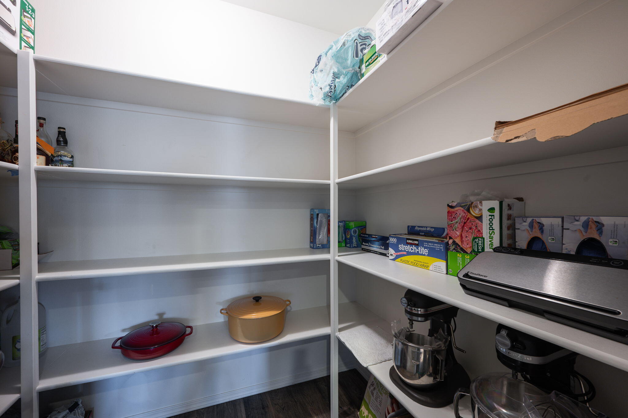 Walk-in pantry with white built-in shelves, cookware, and stand mixers.