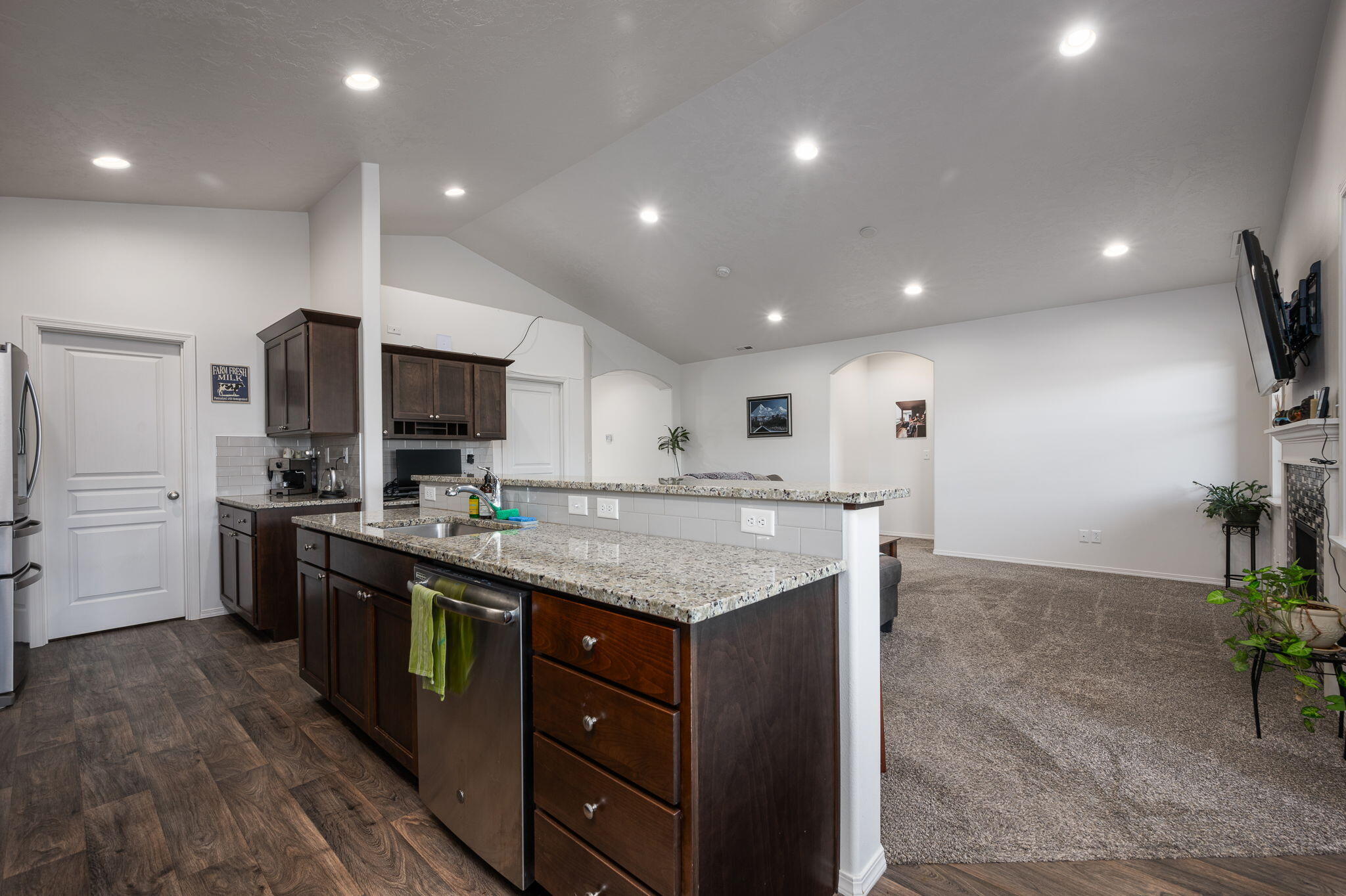 Open-plan kitchen with a granite island and dark wood cabinets beside a carpeted living room.