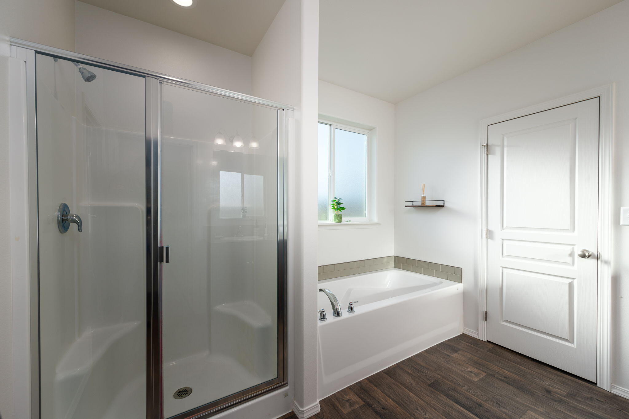Bathroom with a glass-enclosed shower and soaking tub beneath a frosted window.