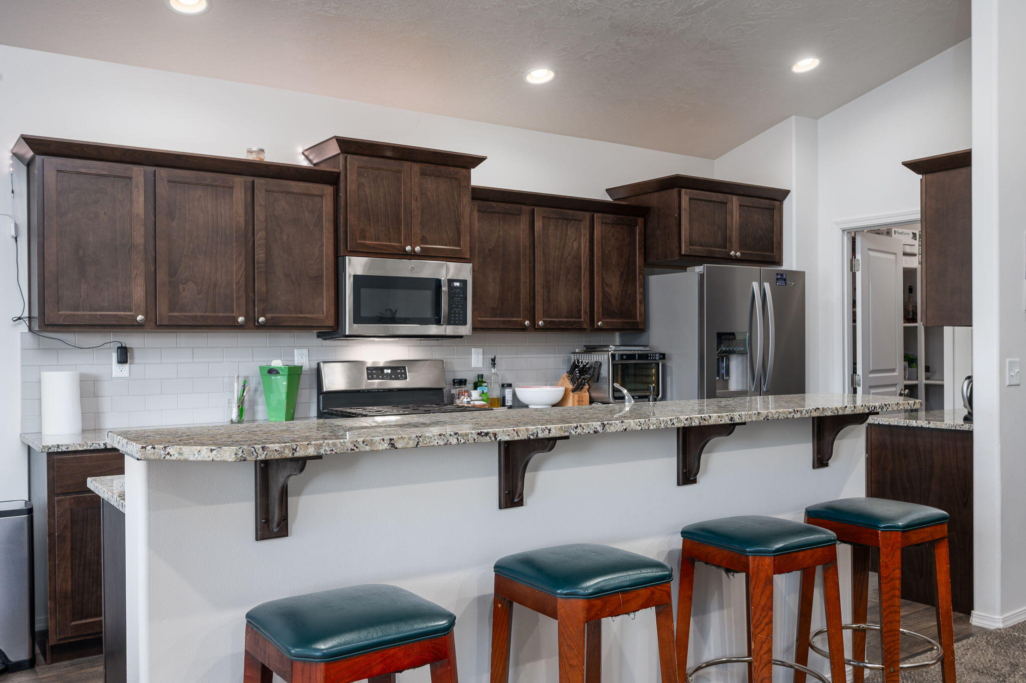 Kitchen with dark wood cabinets, stainless steel appliances, and a granite breakfast bar with stools.