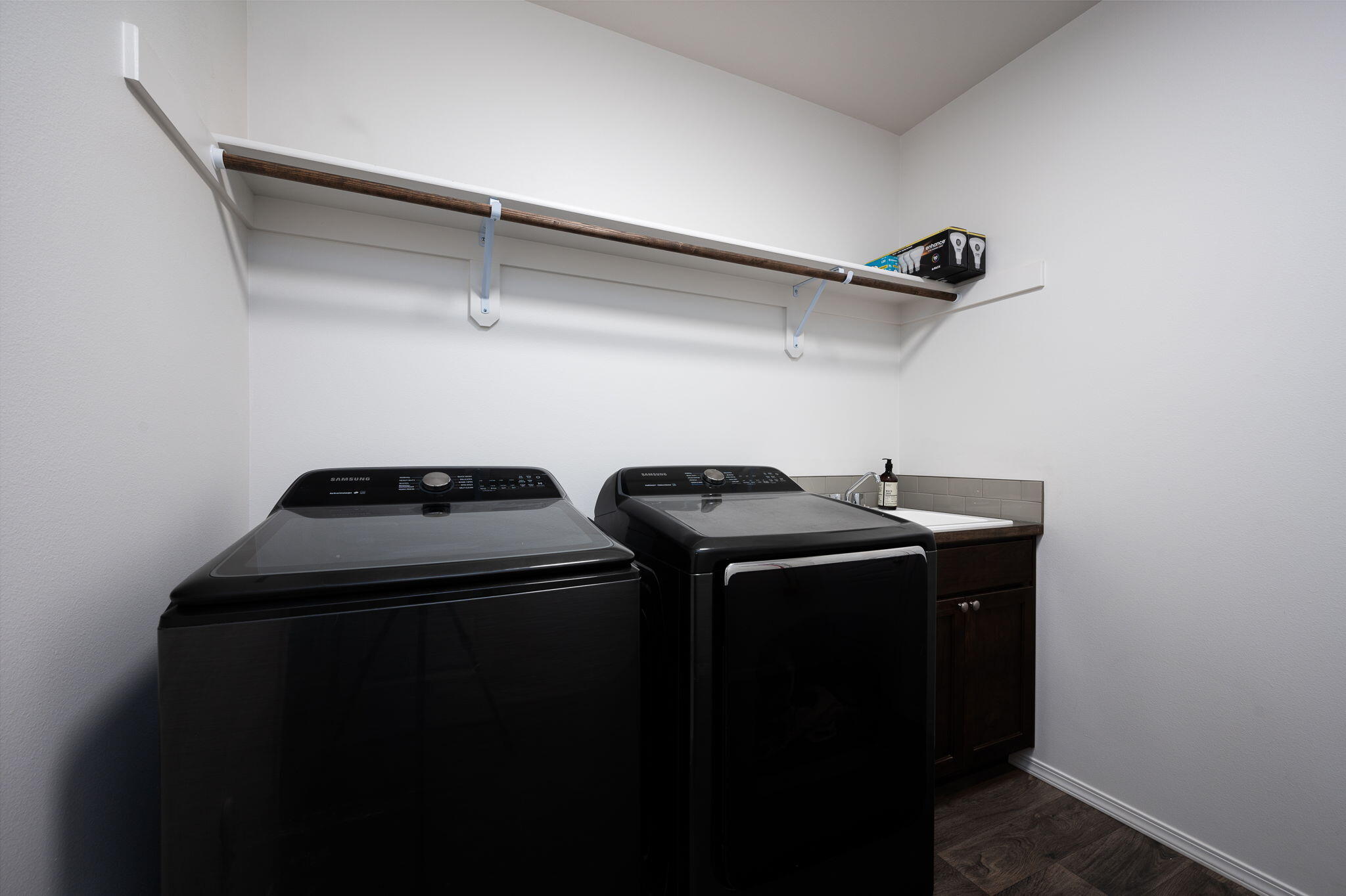 Laundry room with black washer and dryer and a long overhead storage shelf.