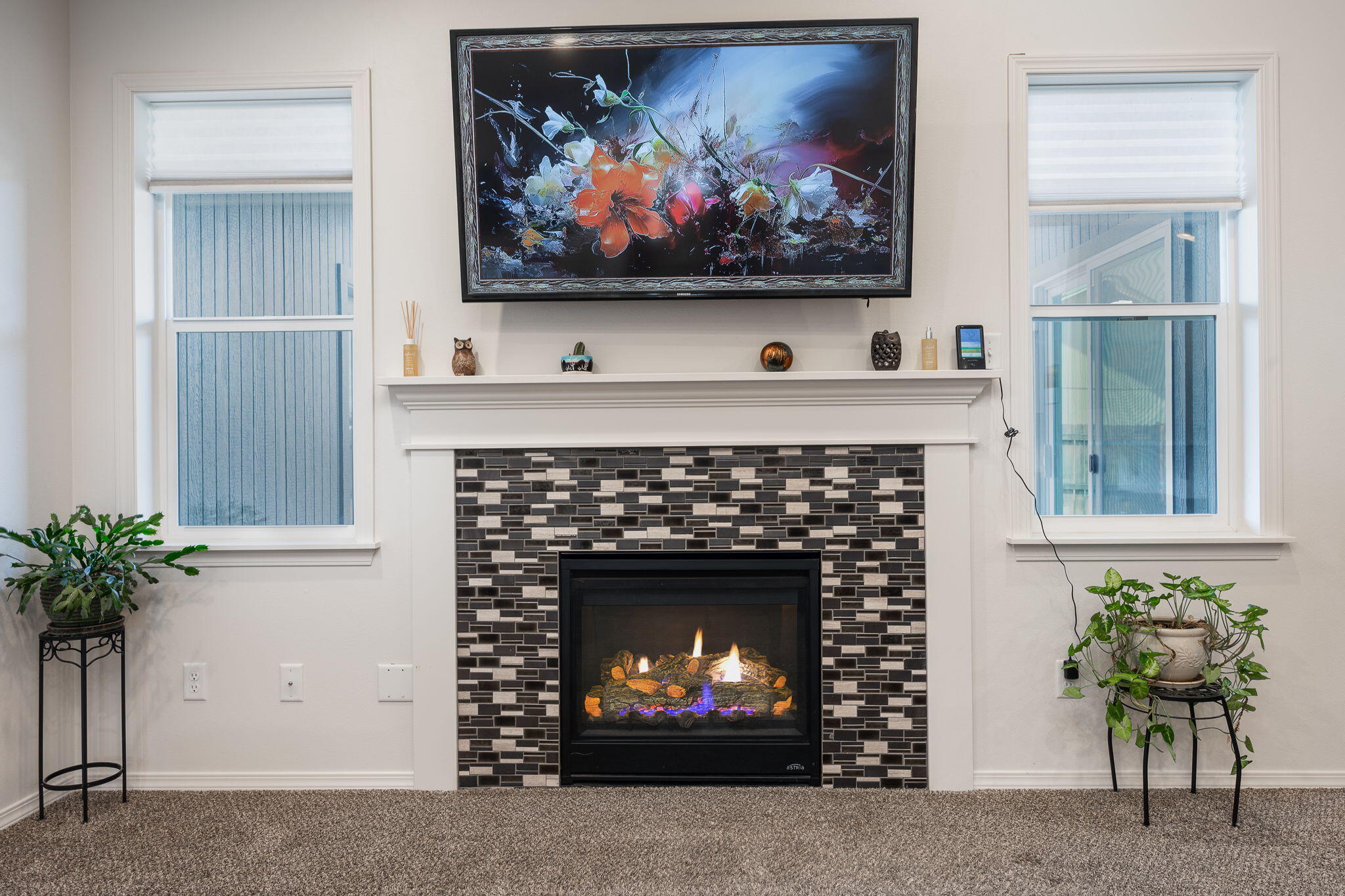 Living room fireplace with a mosaic tile surround, floral artwork, and windows on either side.