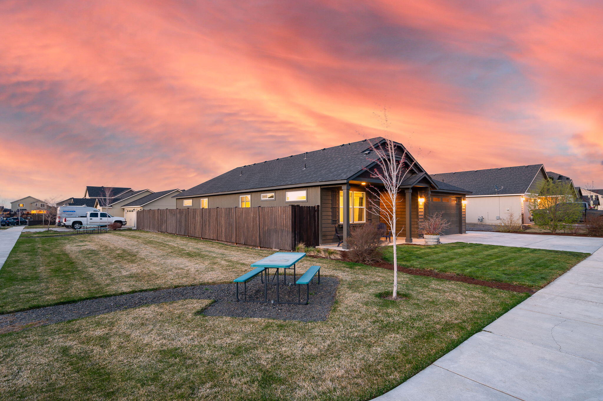 Modern single-story home with a fenced front yard and picnic table at dusk.