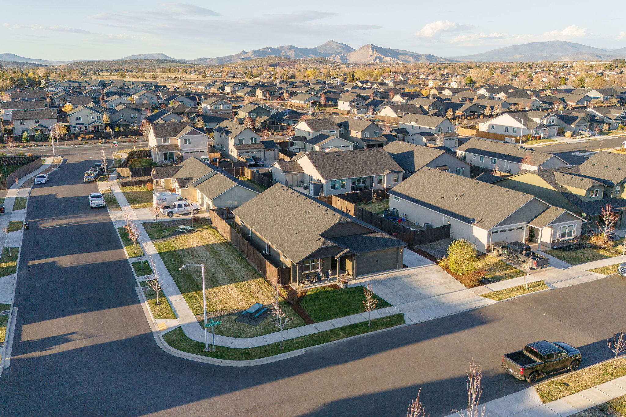 Aerial view of a dark gray corner-lot home, with neighborhood houses and mountains beyond.