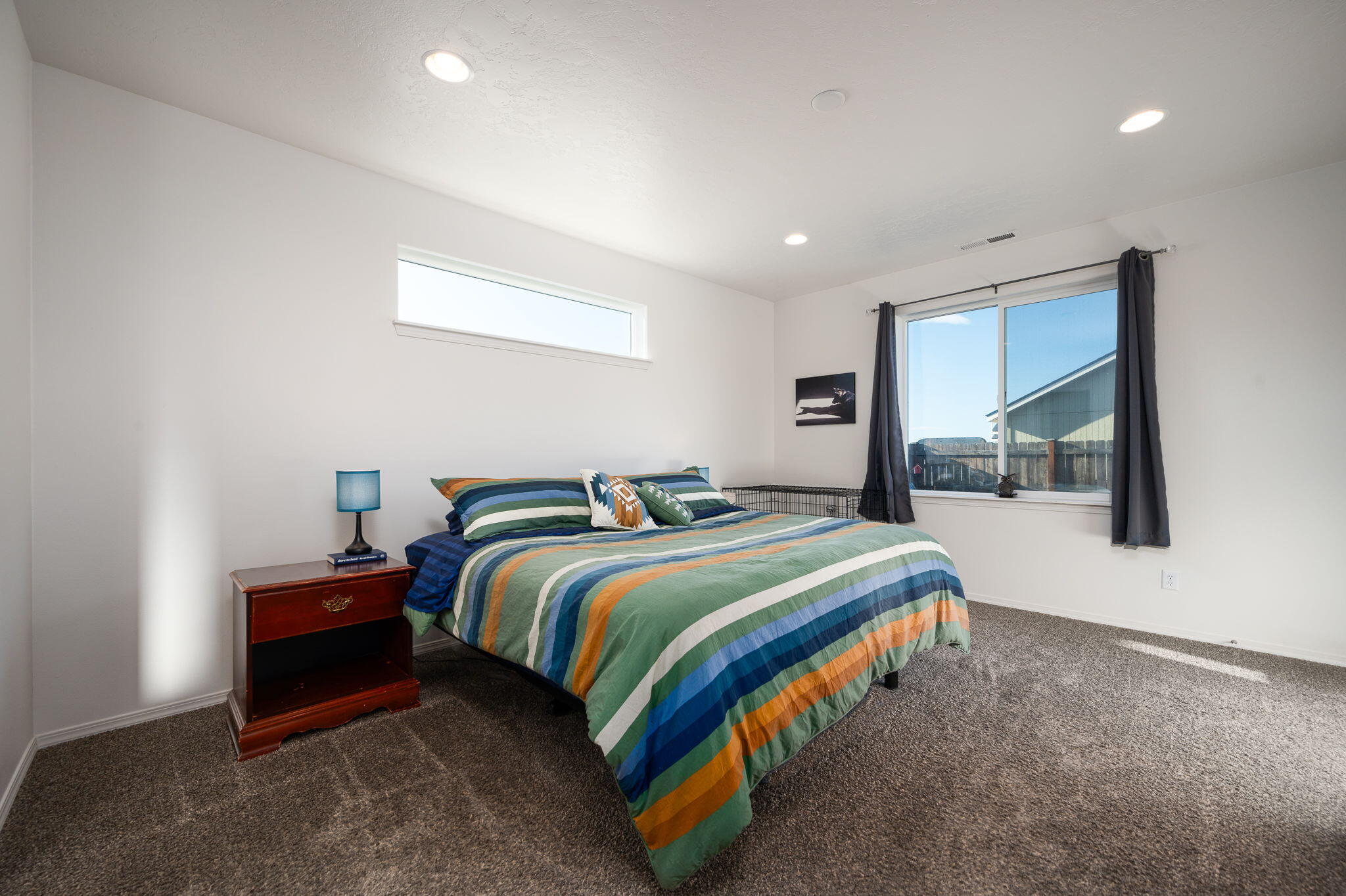 Bedroom with a colorful striped bedspread and a large curtained window.