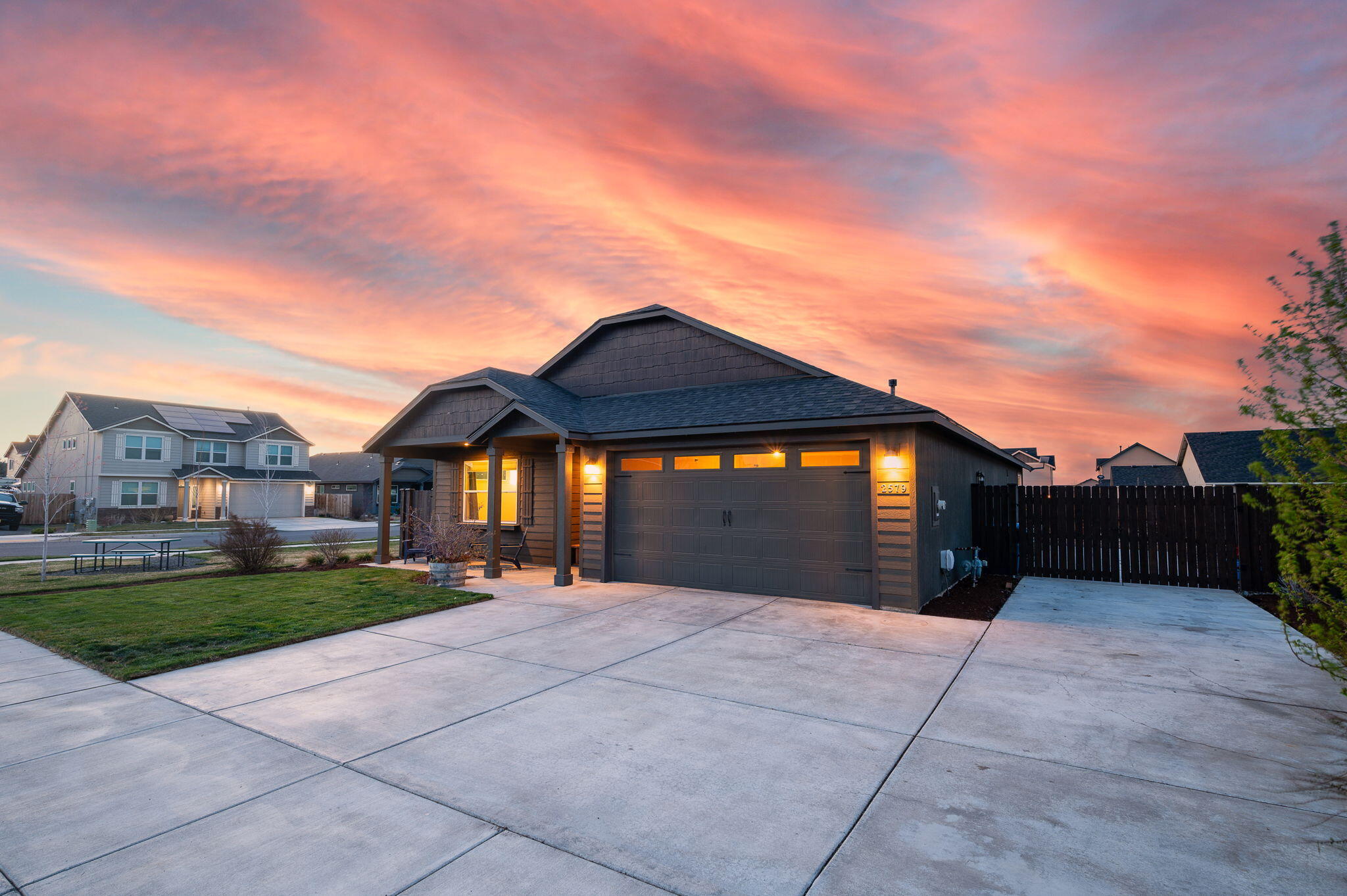 Single-story home with a two-car garage and broad driveway beneath a colorful sunset sky.