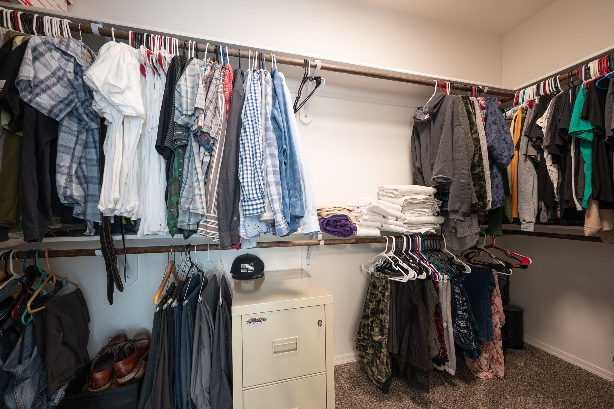 Walk-in closet with clothes on three walls, folded towels, shoes, and a cream-colored safe.