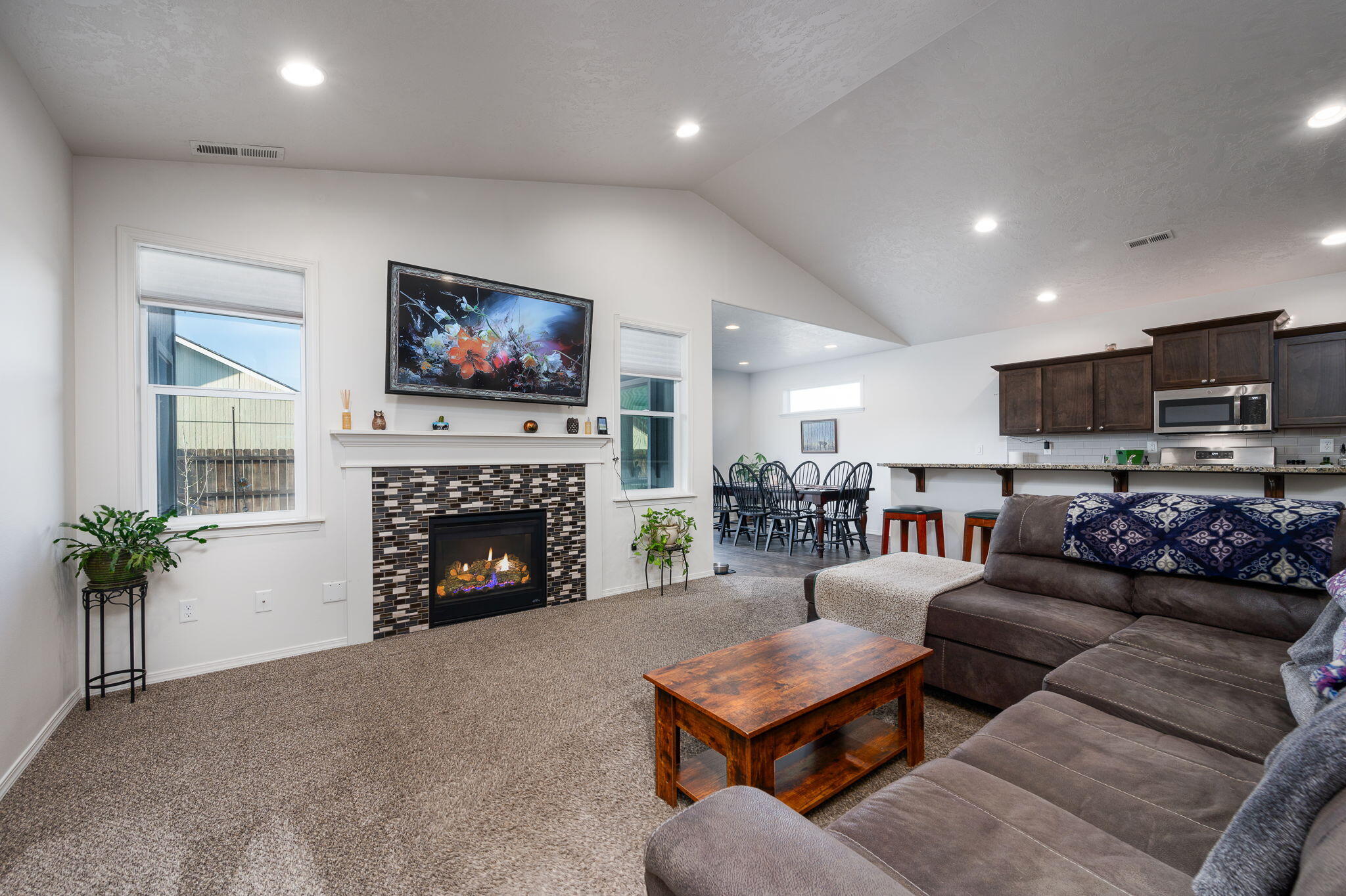 Living room with a tiled gas fireplace, brown sectional, and open dining area and kitchen.