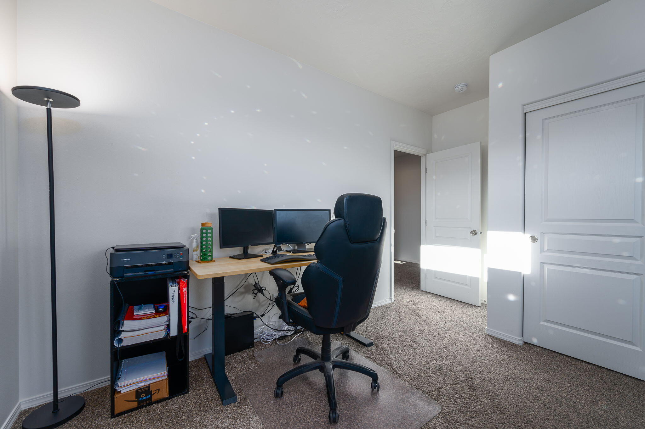 Home office with a dual-monitor desk, black chair, and printer beside open doors.