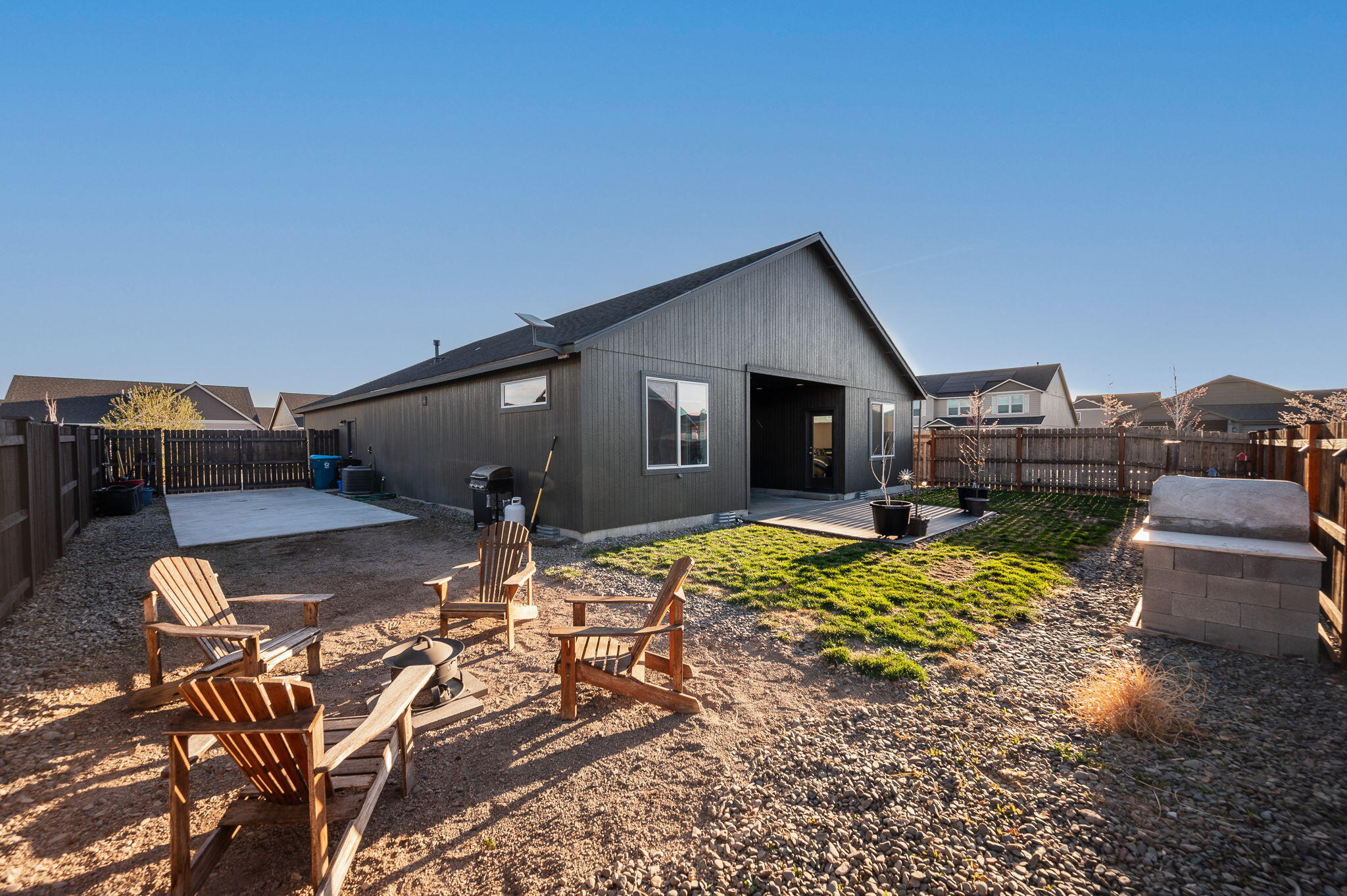 Fenced backyard with Adirondack chairs, a fire pit, gravel landscaping, and a deck beside the home.