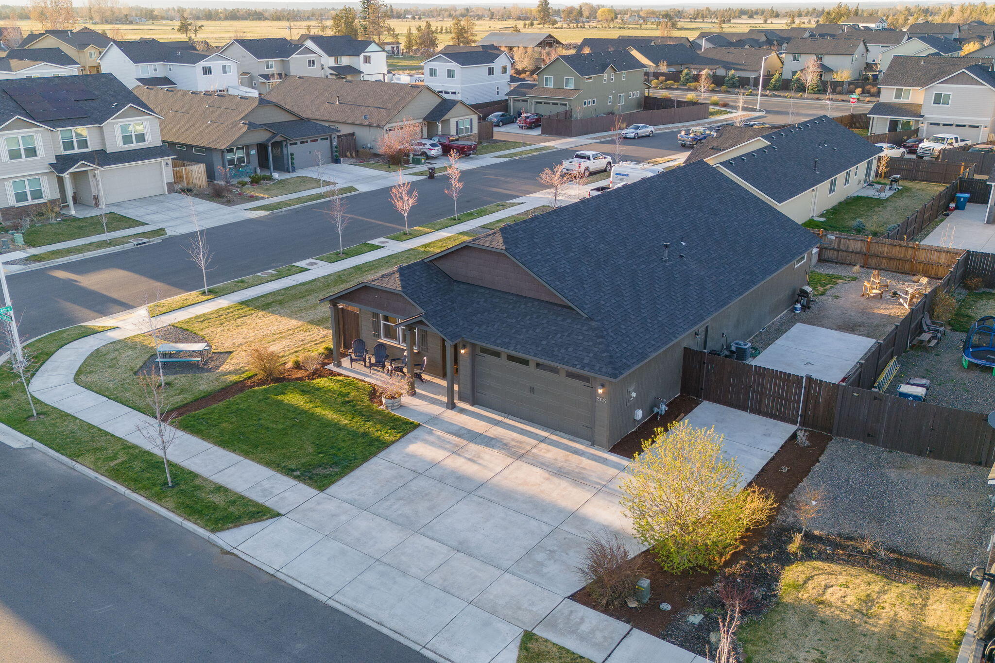 Aerial view of a dark gray single-story home with a large garage, covered porch, and fenced yard.