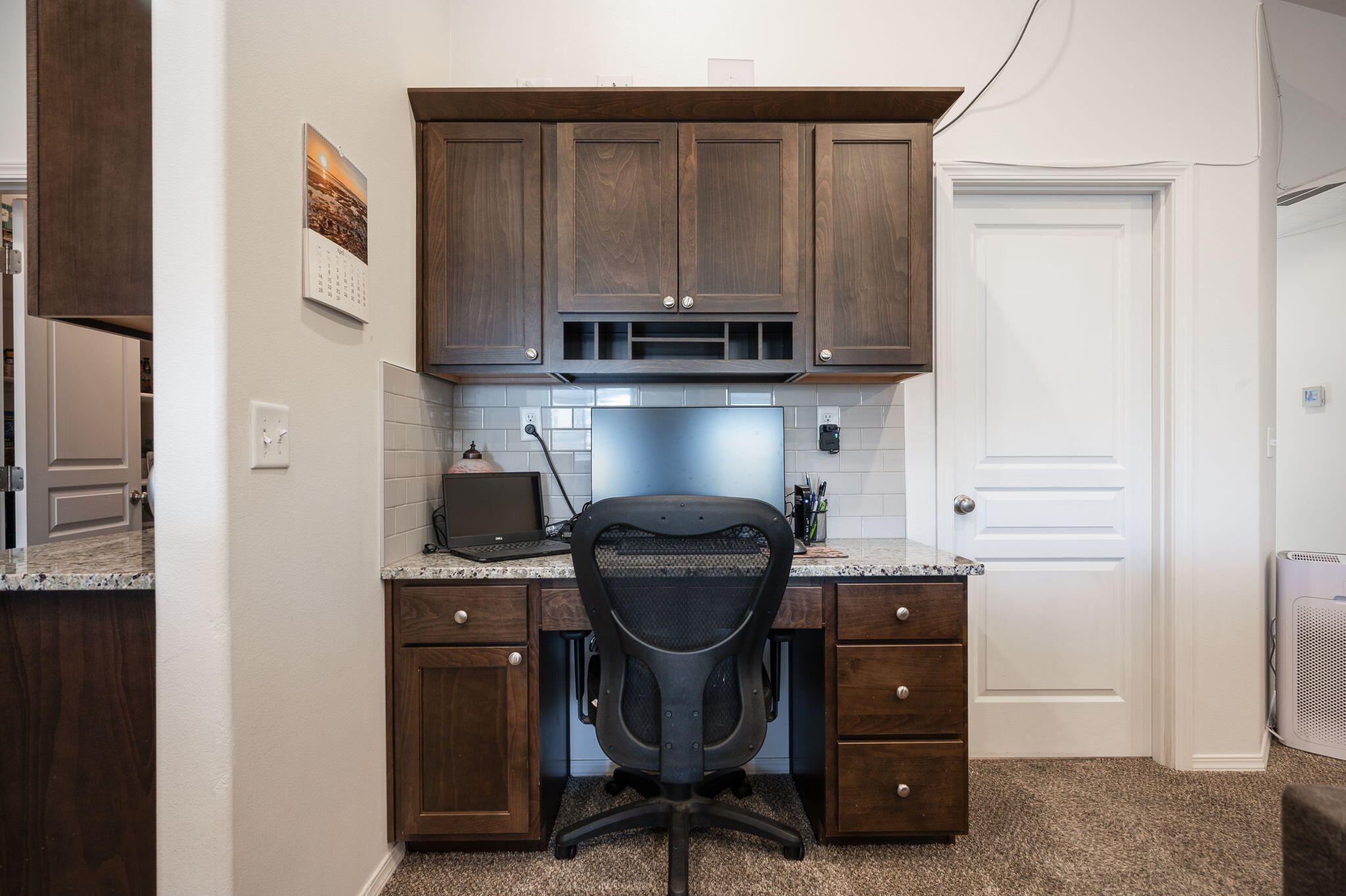 Home office with dark wood built-in cabinetry, desk, computer, and black office chair.