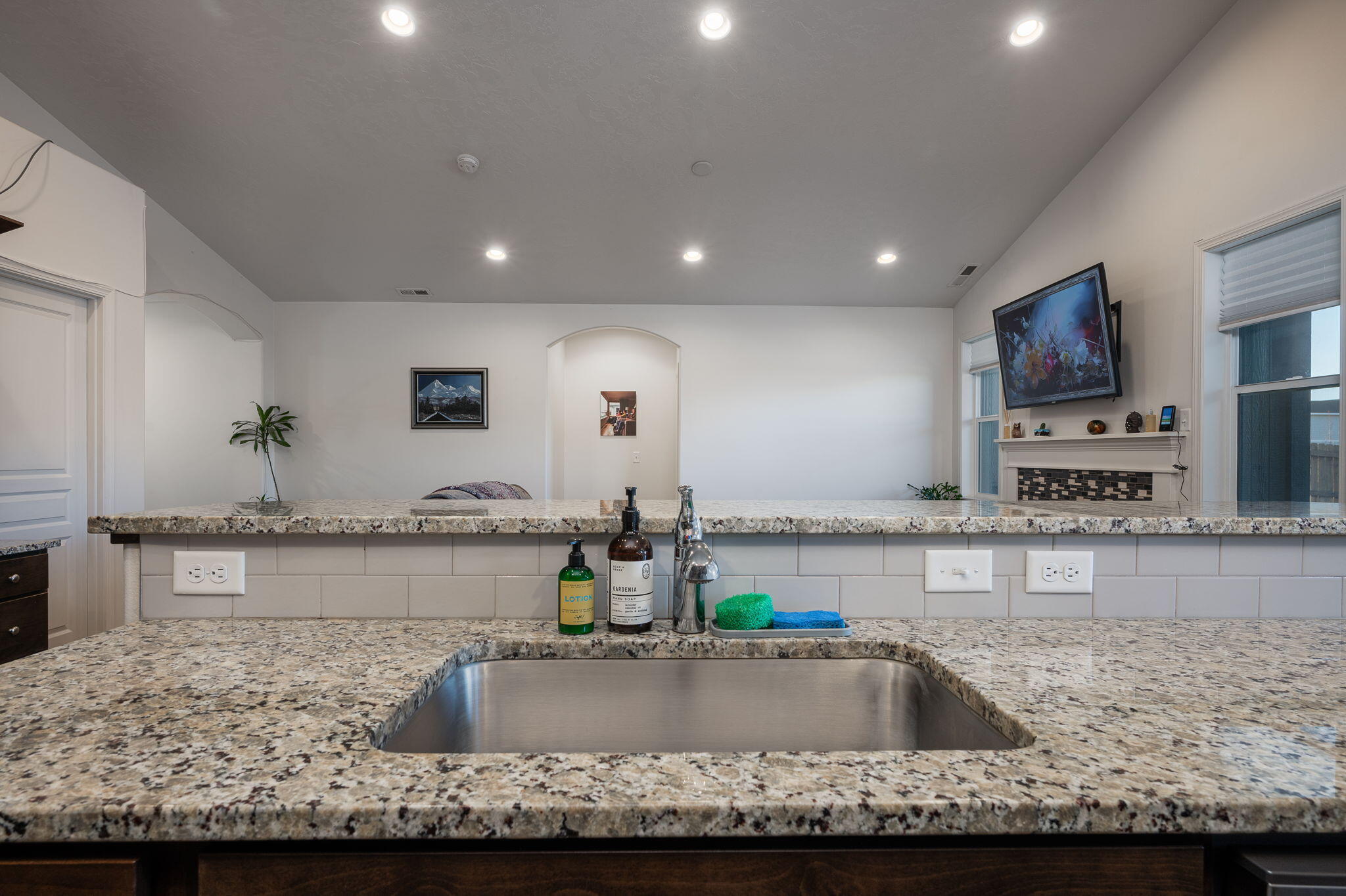 Kitchen with a large stainless-steel sink and granite counters, opening toward a living area with a fireplace.