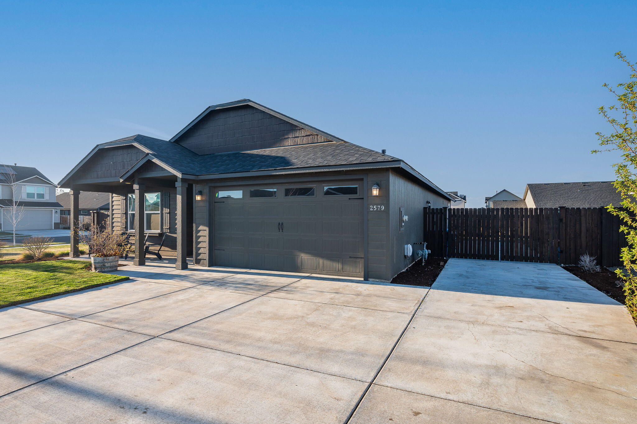 Dark gray home with a two-car garage, covered porch, broad driveway, and fenced side yard.