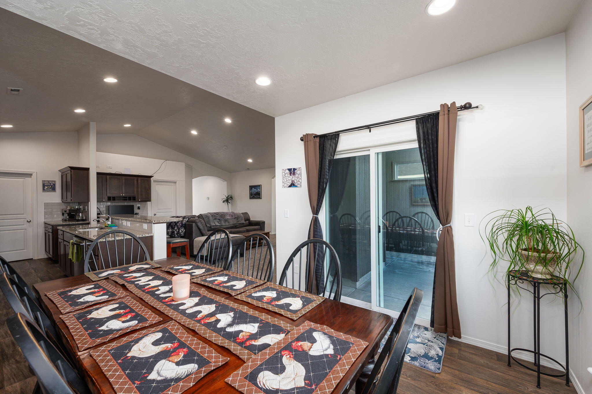 Dining area with rooster-patterned placemats, open to a kitchen and living room.