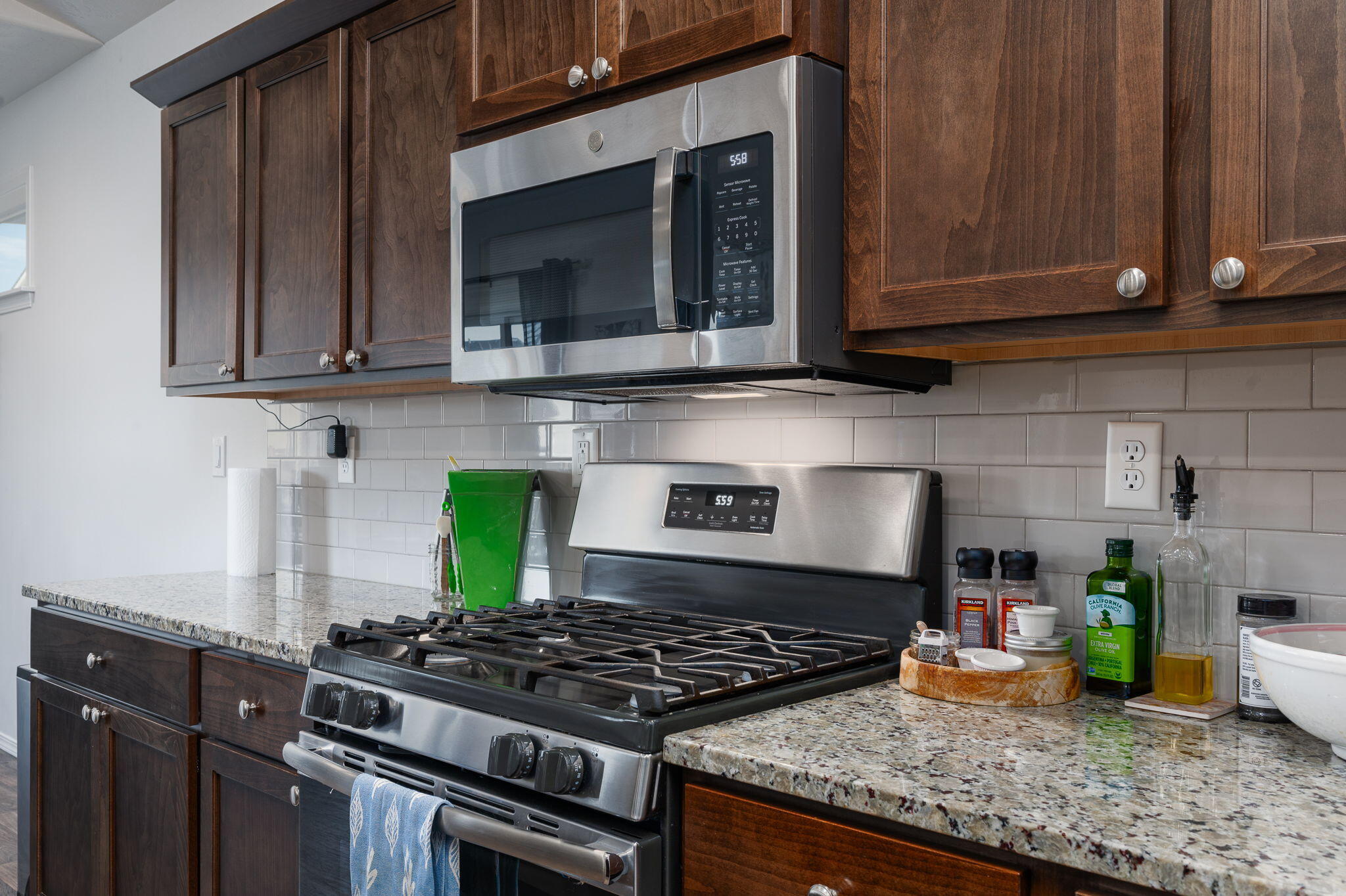 Kitchen with dark wood cabinets, granite counters, and stainless steel gas range and microwave.