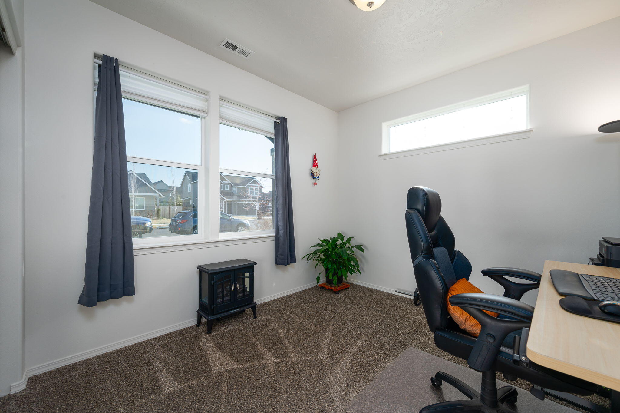 Home office with curtained windows, desk, black office chair, and potted plant.