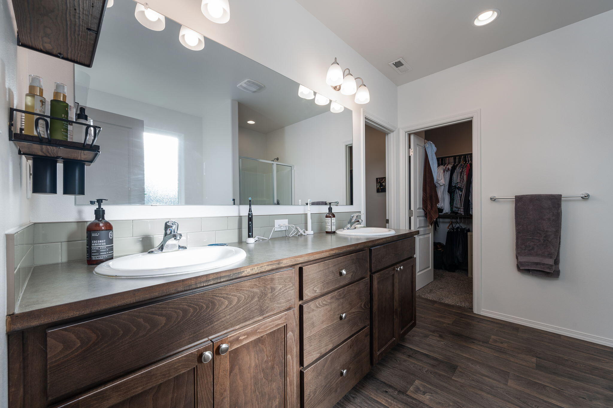 Bathroom with a dark wood double vanity, broad mirror, glass shower, and open walk-in closet.