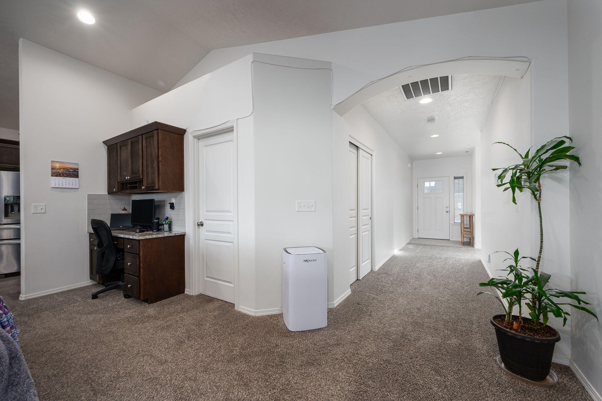 Carpeted entry hallway with a built-in desk, arched ceiling detail, and large potted plant.