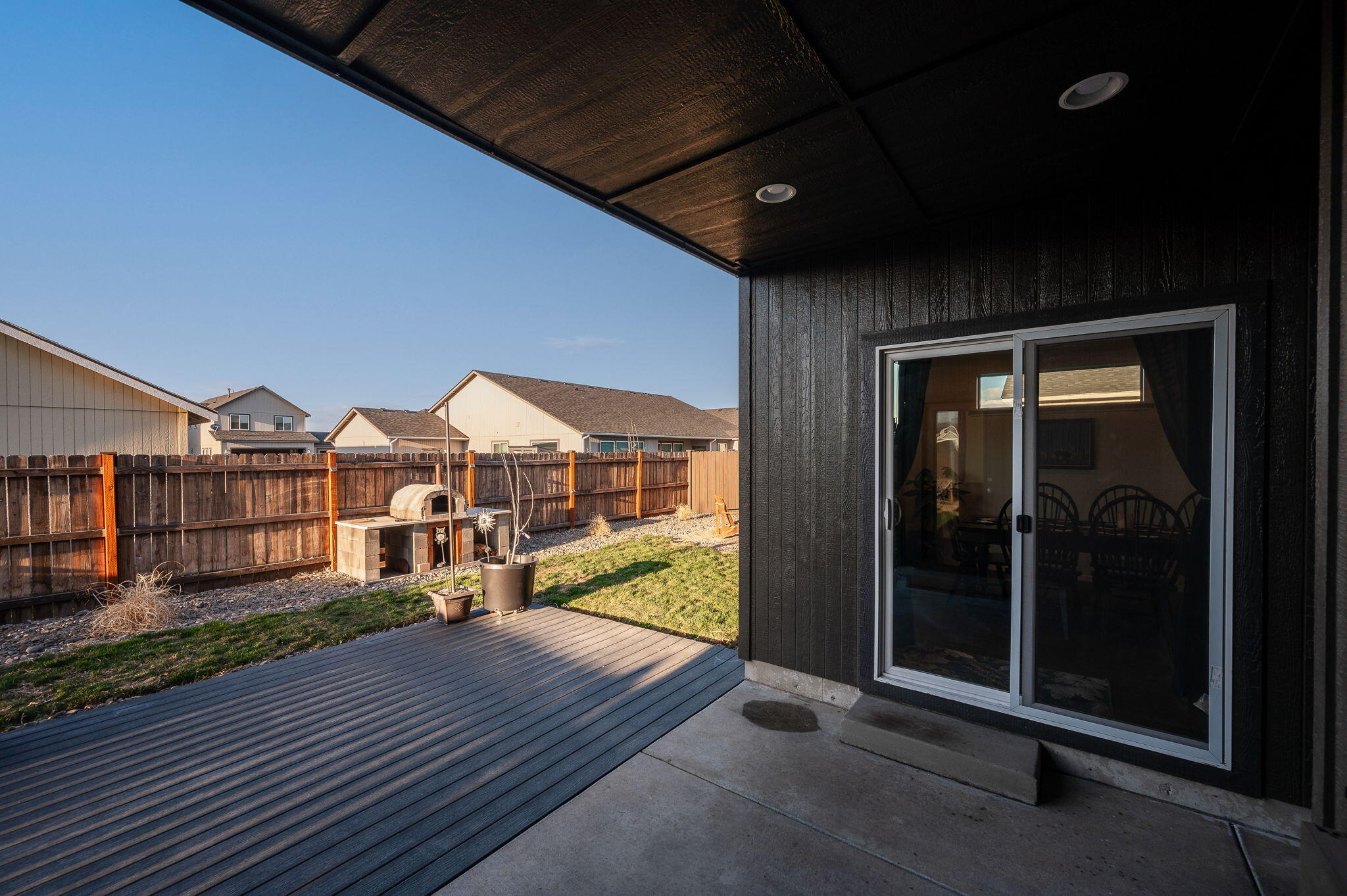 Covered patio and composite deck beside a fenced grassy backyard with a small outdoor oven.