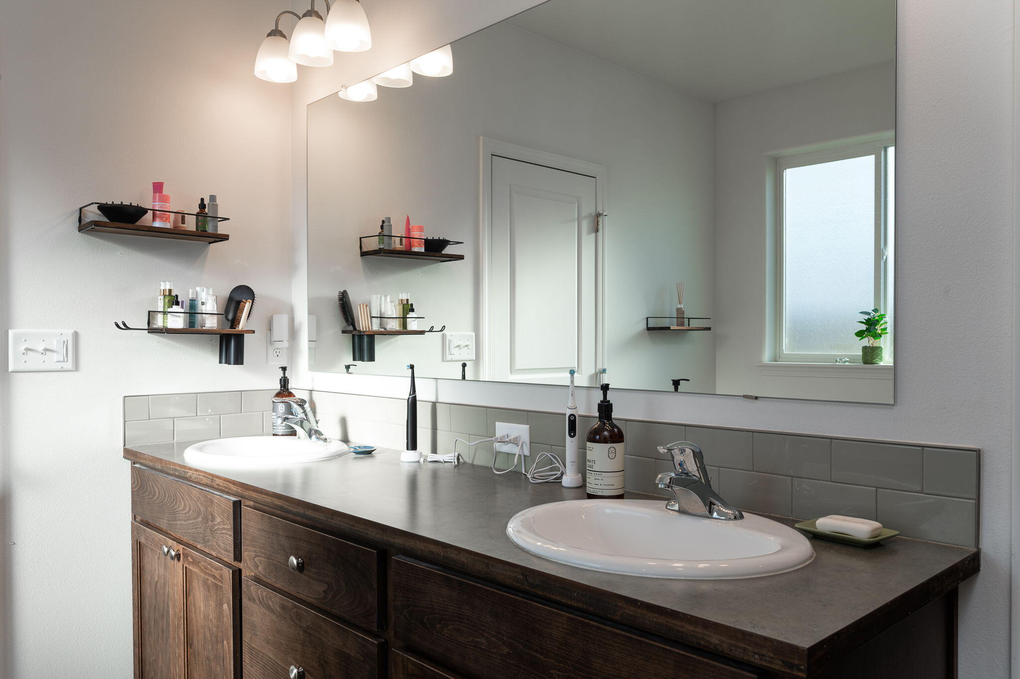 Bathroom with a dark wood double vanity, two white sinks, gray tile backsplash, and a large mirror.