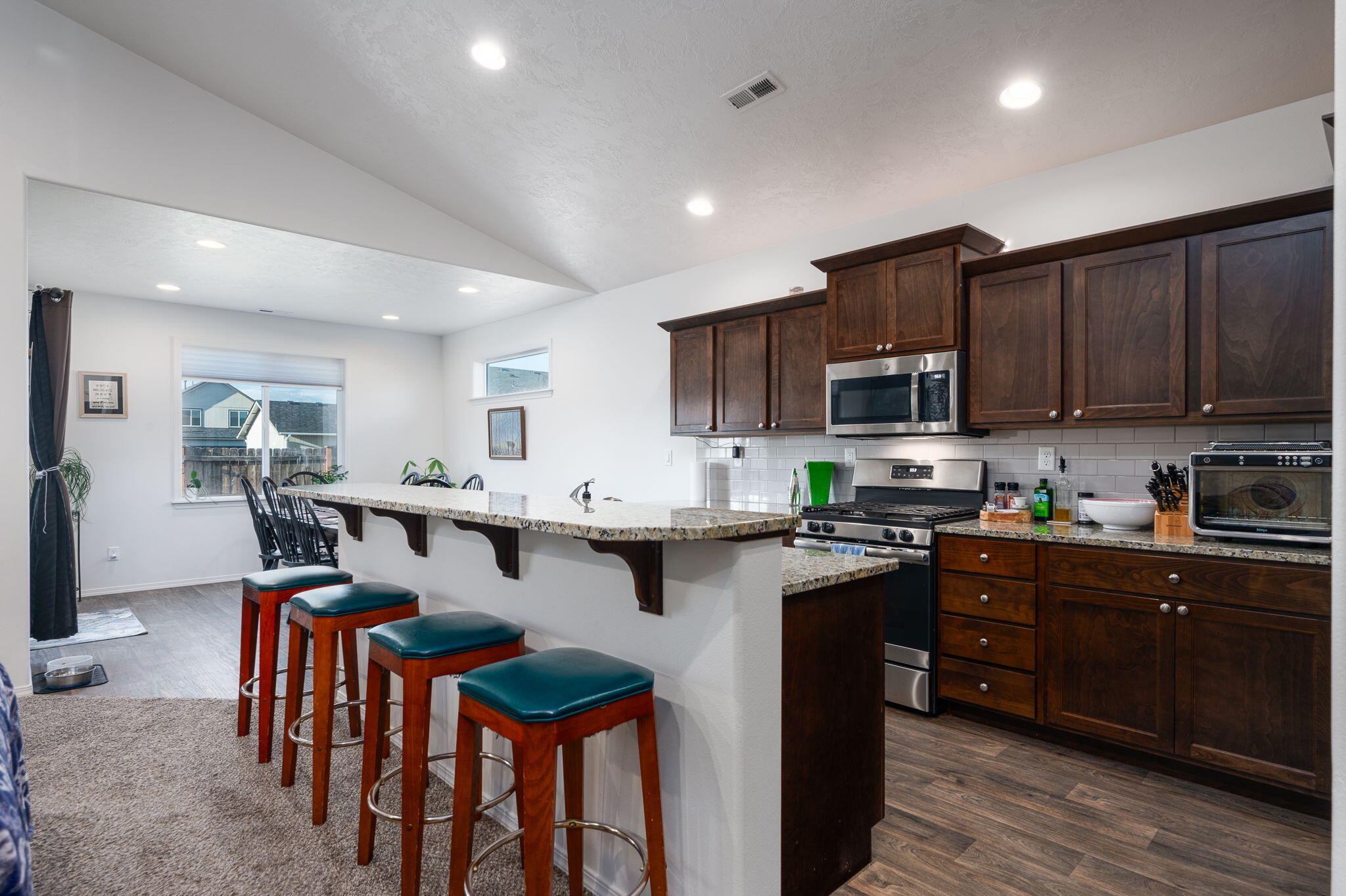 Kitchen with dark wood cabinets, stainless steel appliances, and a long granite breakfast bar with four stools.