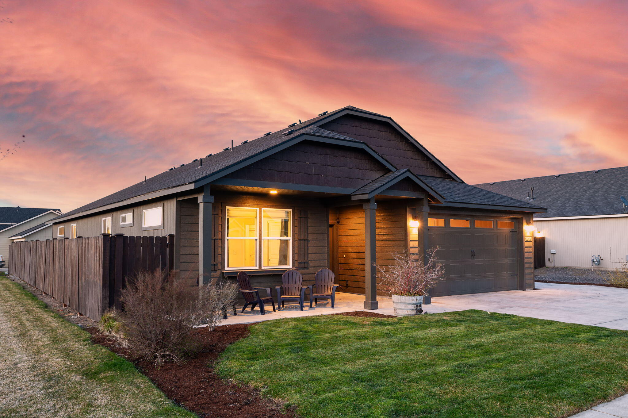 Dark-sided house with a covered porch and attached garage at dusk beneath a pink sky.
