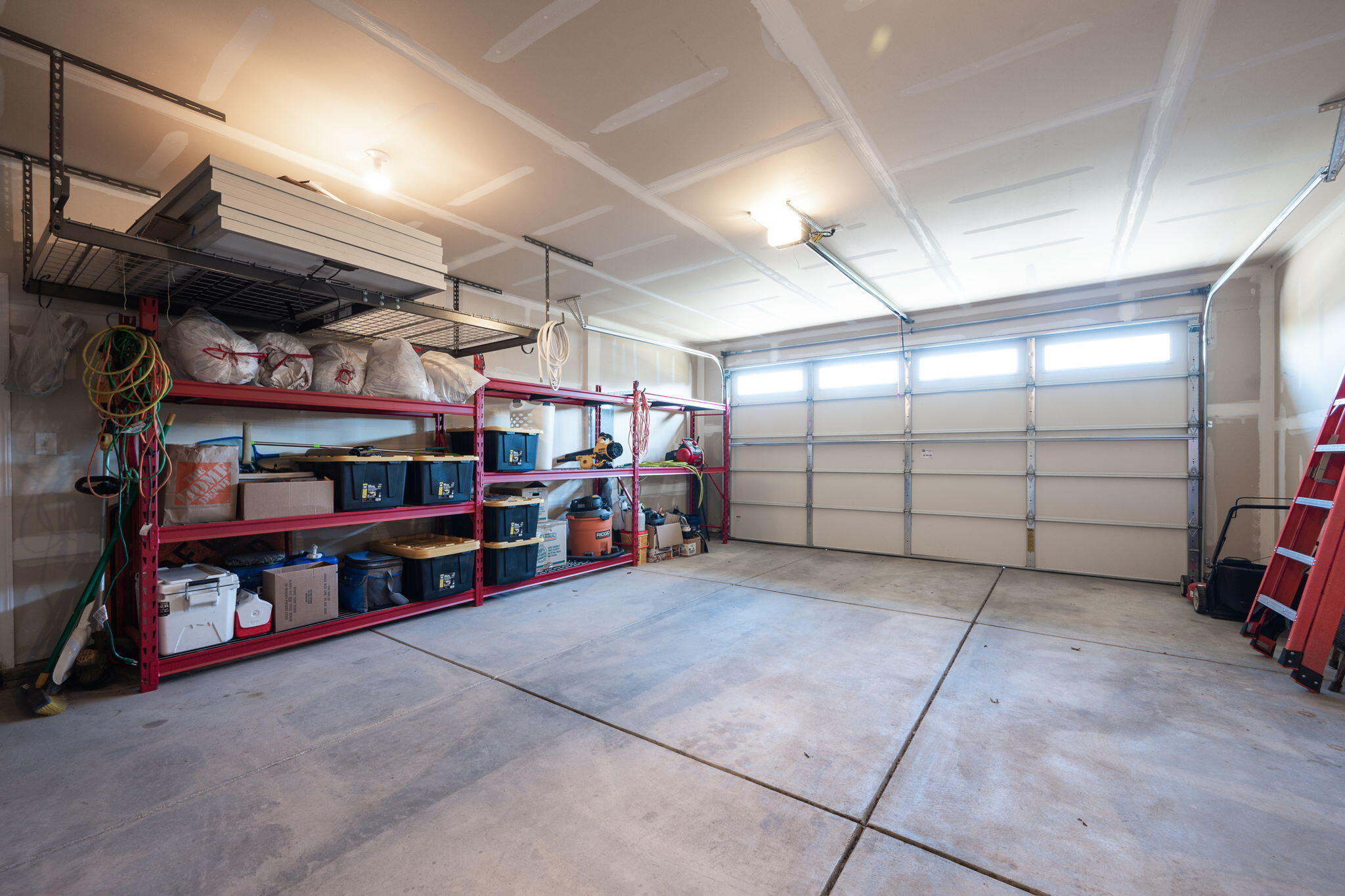 Garage with red storage shelves, ceiling racks, and a closed sectional door.