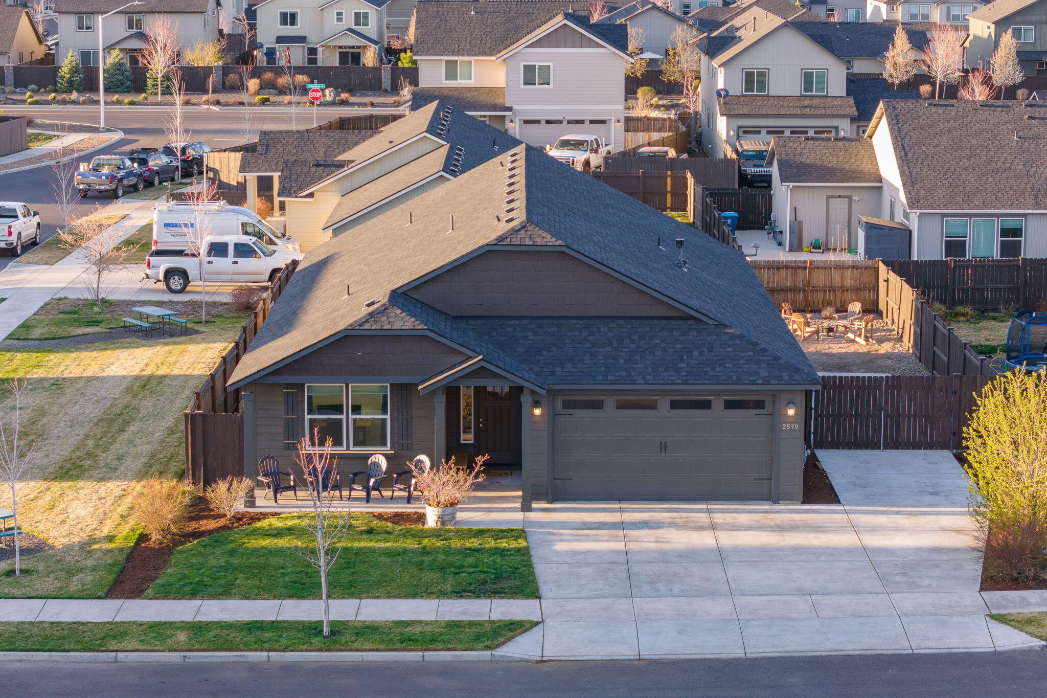 Dark gray home with a two-car garage, covered porch seating, fenced yard, and wide driveway.