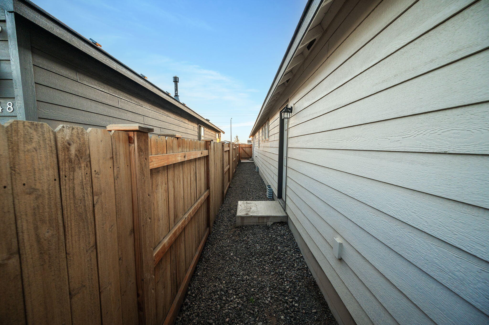 Gravel side passage beside a light-sided house, enclosed by a tall wooden privacy fence.