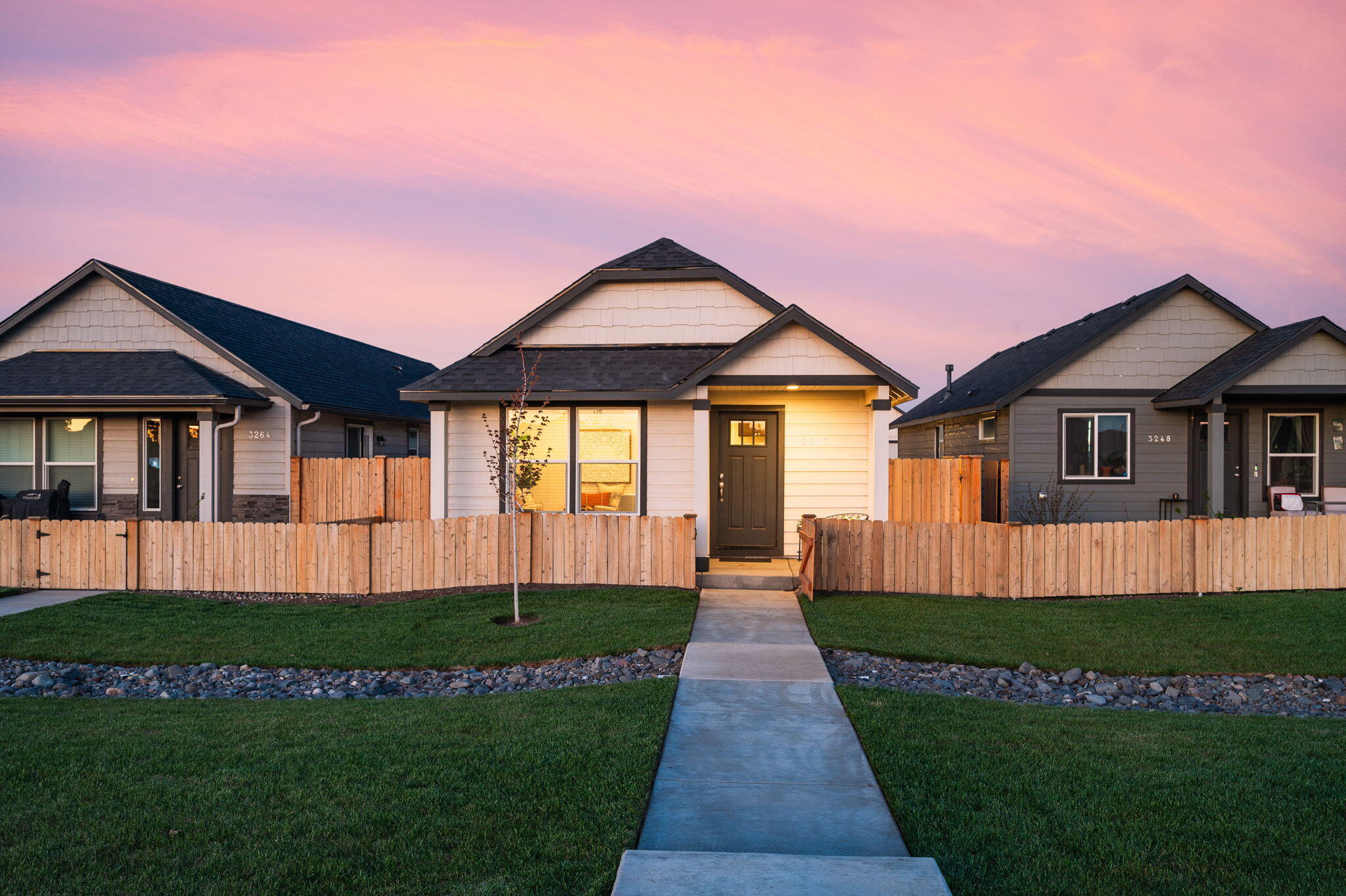 Single-story home with a fenced lawn, concrete entry walkway, and illuminated windows at dusk.