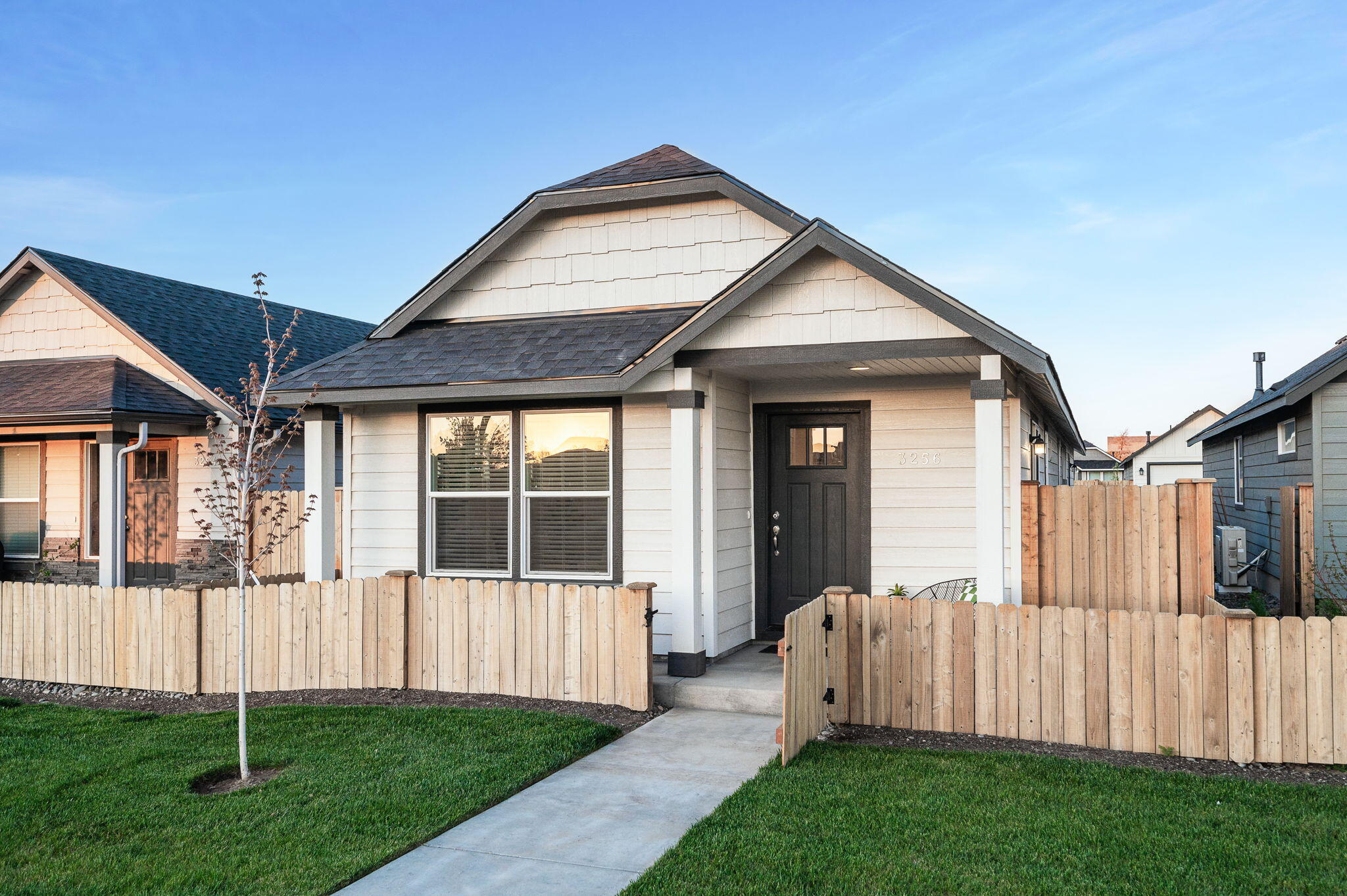 House with light siding, dark gabled roof, and wooden front fence at golden hour.