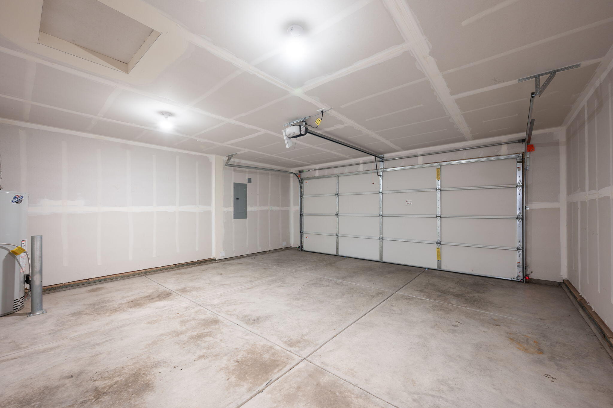 Empty garage with concrete floor, unfinished drywall, closed garage door, and overhead opener.
