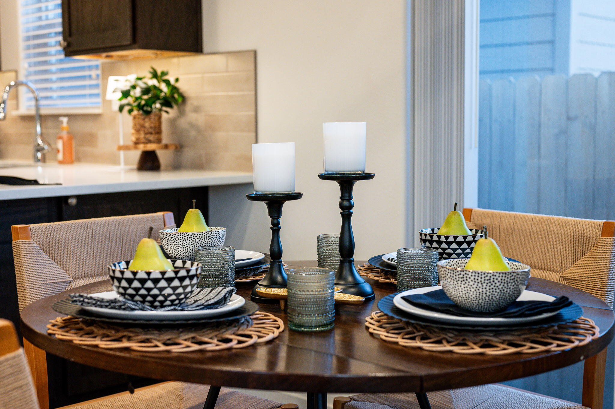 Dining table set with patterned dishes, pears and candleholders beside the kitchen.