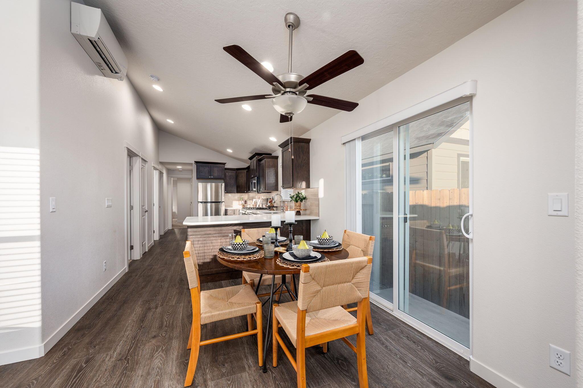 Dining area with a set table beside a sliding glass door, opening to a kitchen with dark cabinets.