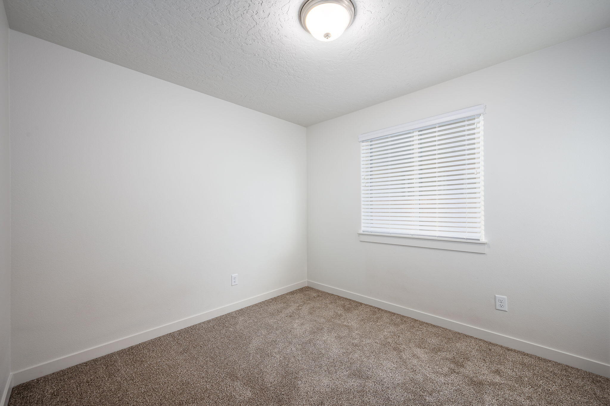Empty carpeted room with white walls and a window fitted with blinds.