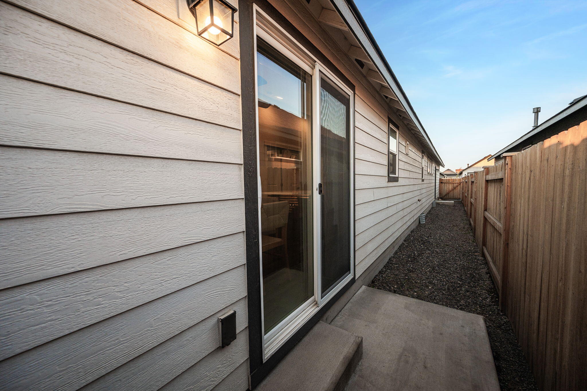 Home’s side patio with a sliding glass door and fenced gravel walkway.