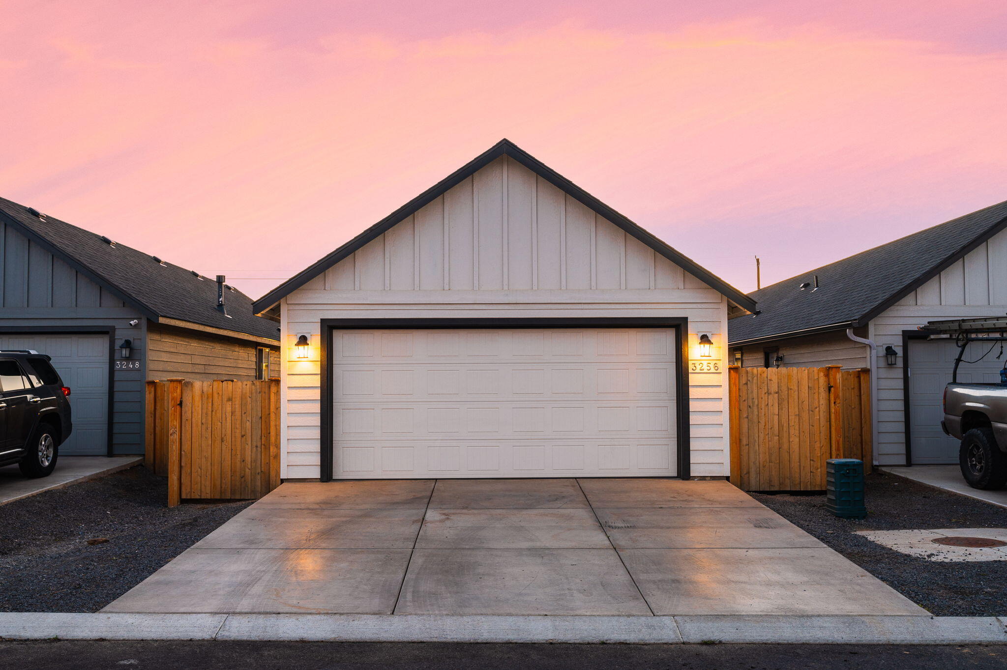 Home exterior with a wide double garage, wooden side fences, and driveway beneath a pink dusk sky.