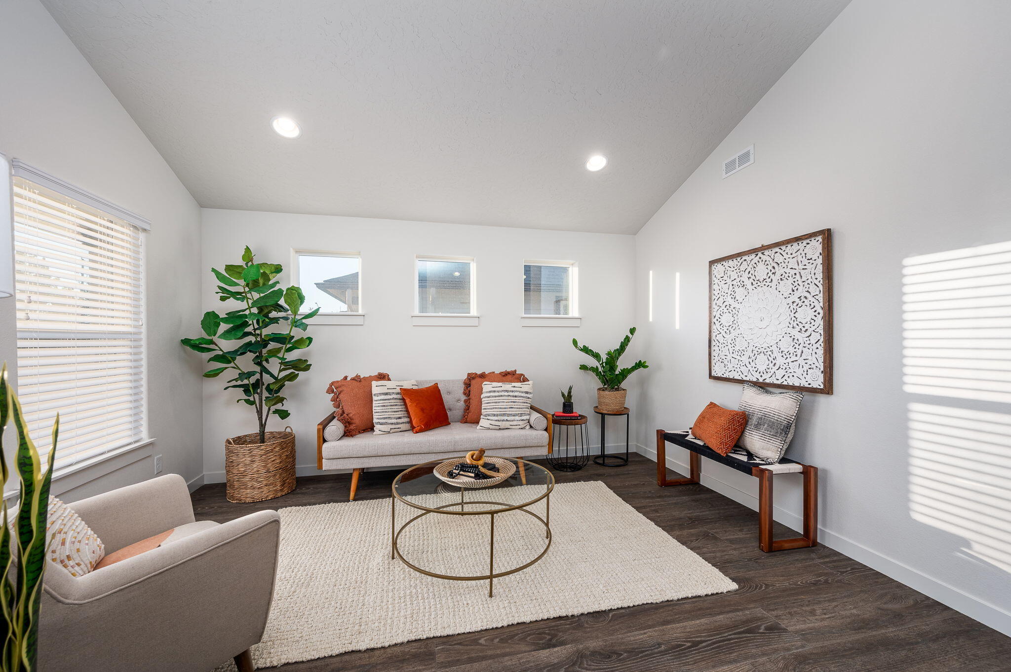 Staged living room with a sloped ceiling, rust-accented sofa, plants, and round glass coffee table.