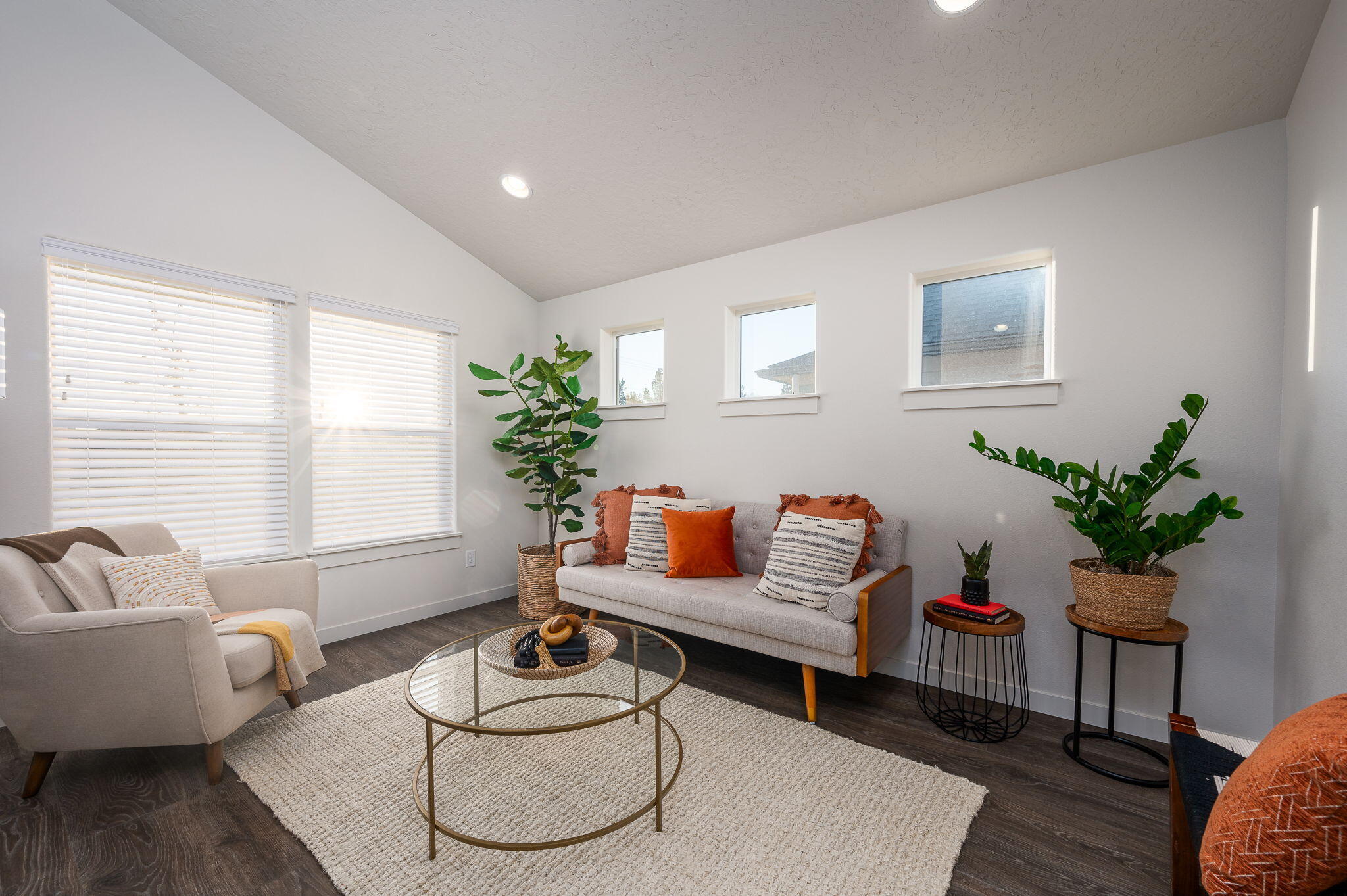 Staged living room with a sloped ceiling, bright windows, neutral sofas, potted plants, and a glass coffee table.