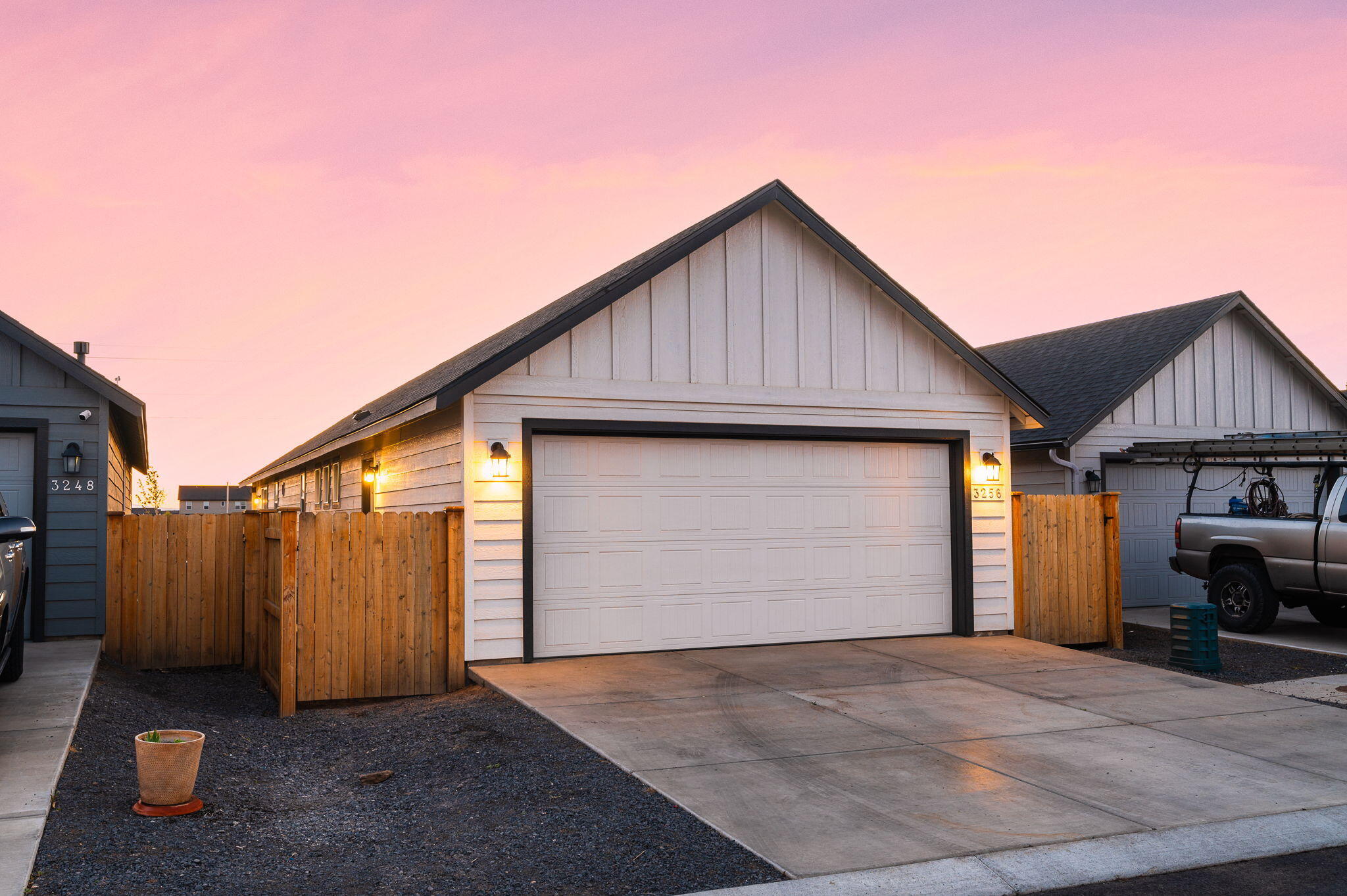 Home exterior with a white gabled facade, double garage, and wooden fencing at dusk.