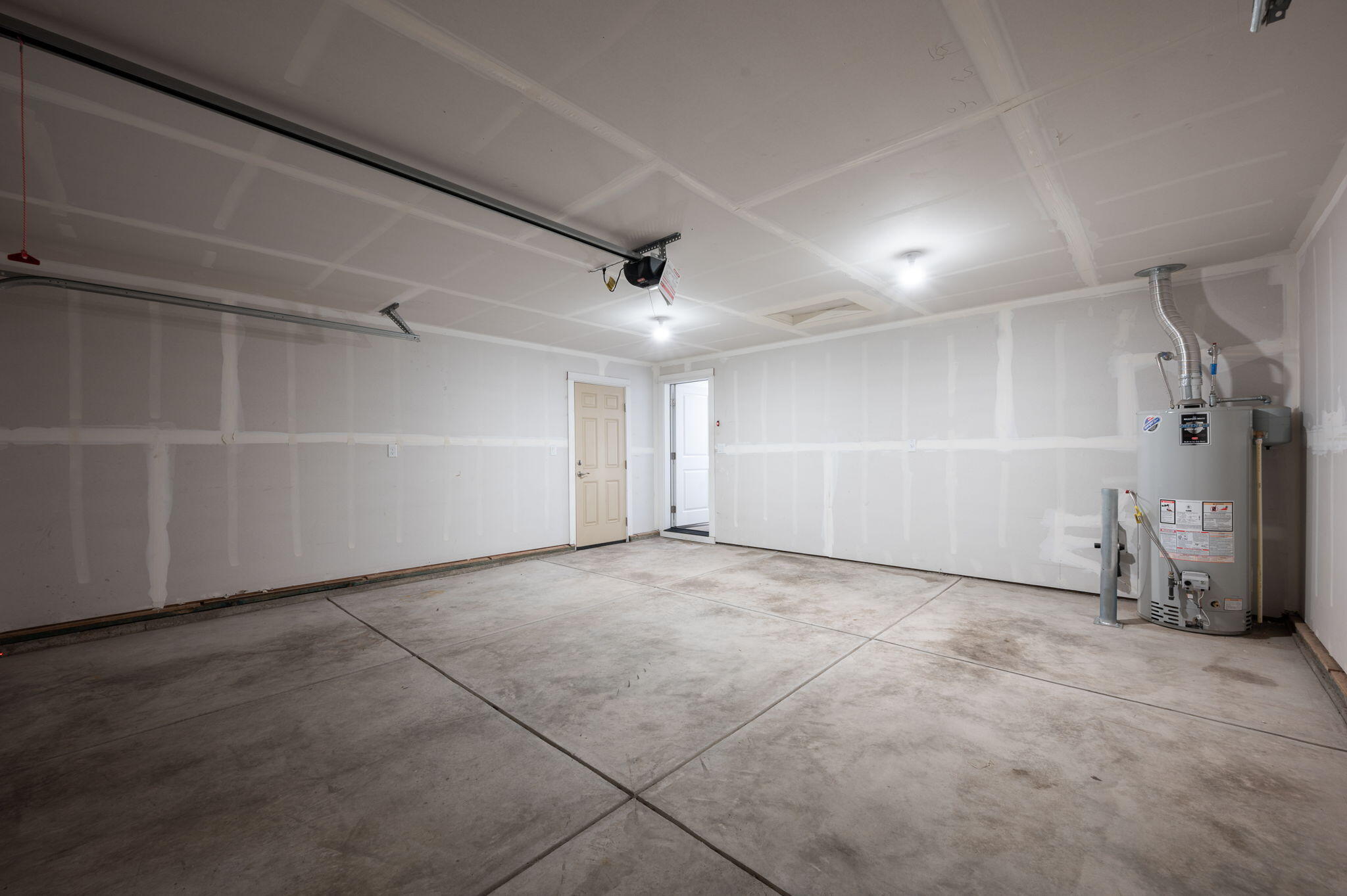 Empty garage with unfinished drywall, concrete floor, and a water heater.