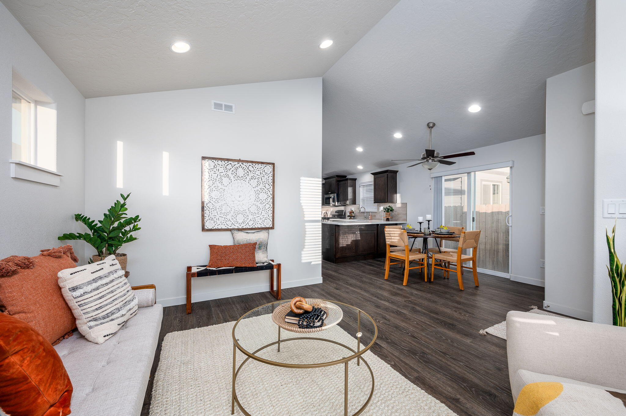 Open-plan living room with a round glass coffee table, dining area, and dark-cabinet kitchen.