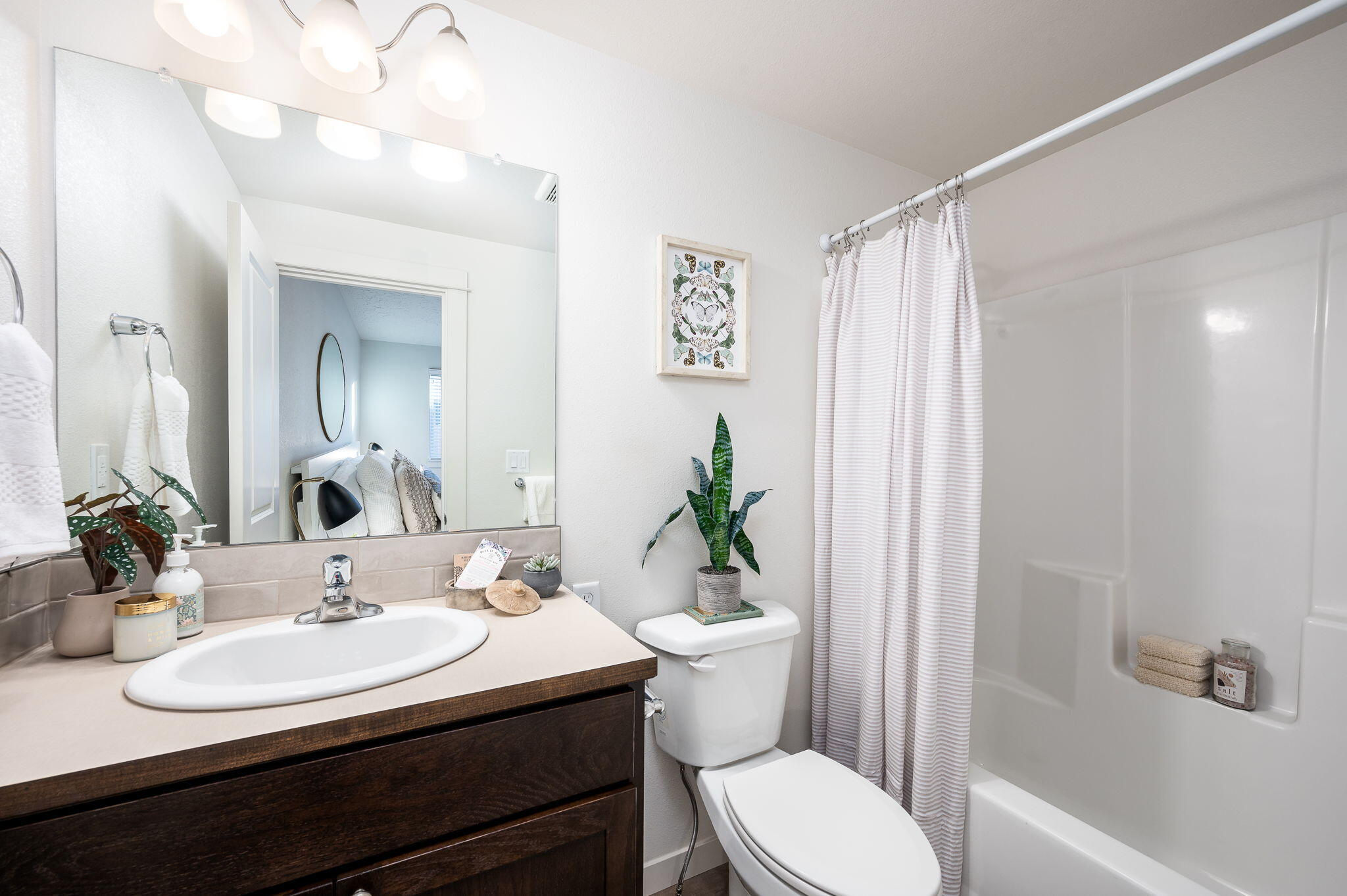 Bathroom with a dark wood vanity, large mirror, and bathtub behind a striped shower curtain.