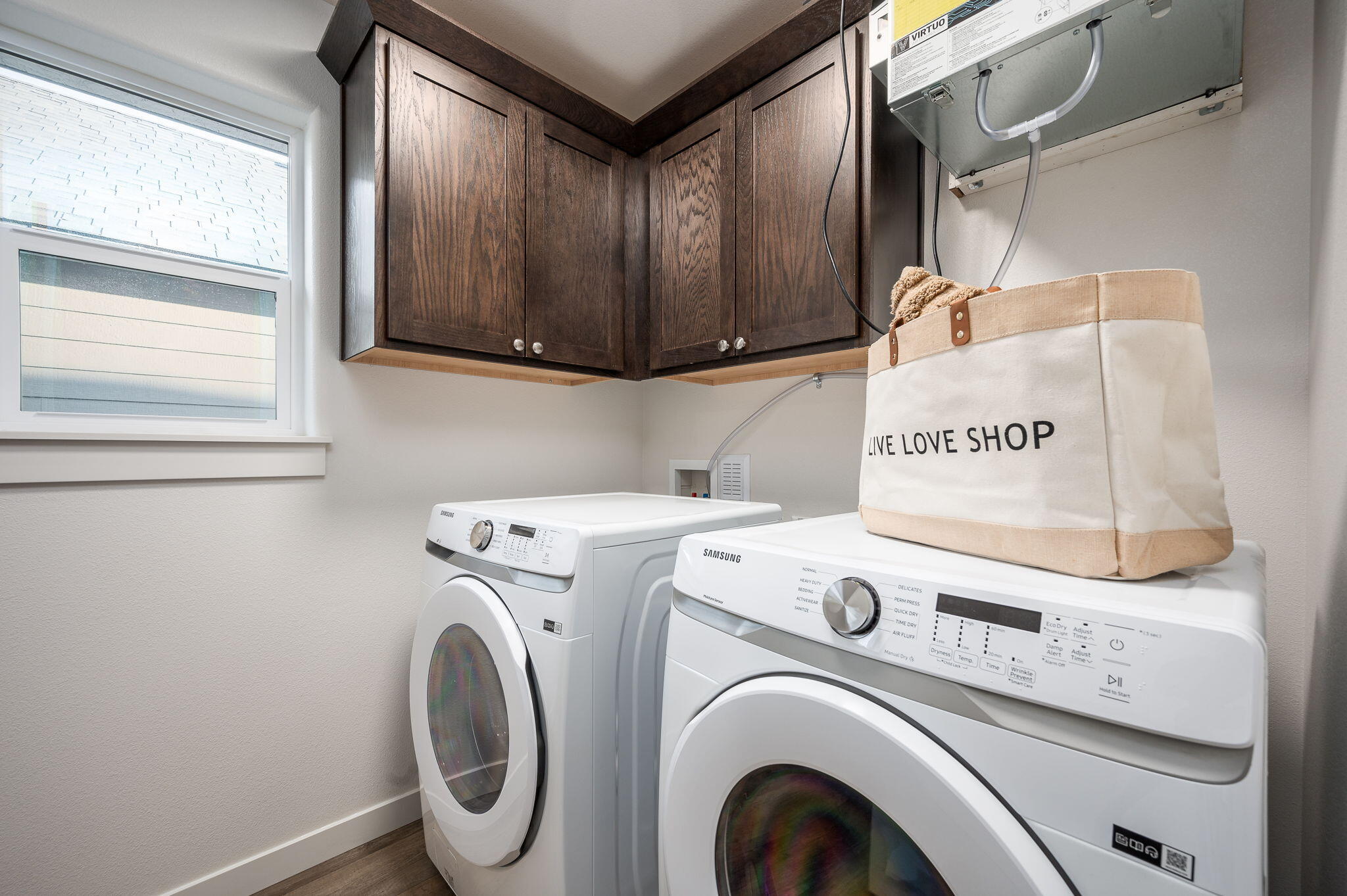 Laundry room with front-loading washer and dryer, dark wood cabinets, and a canvas bag on the dryer.