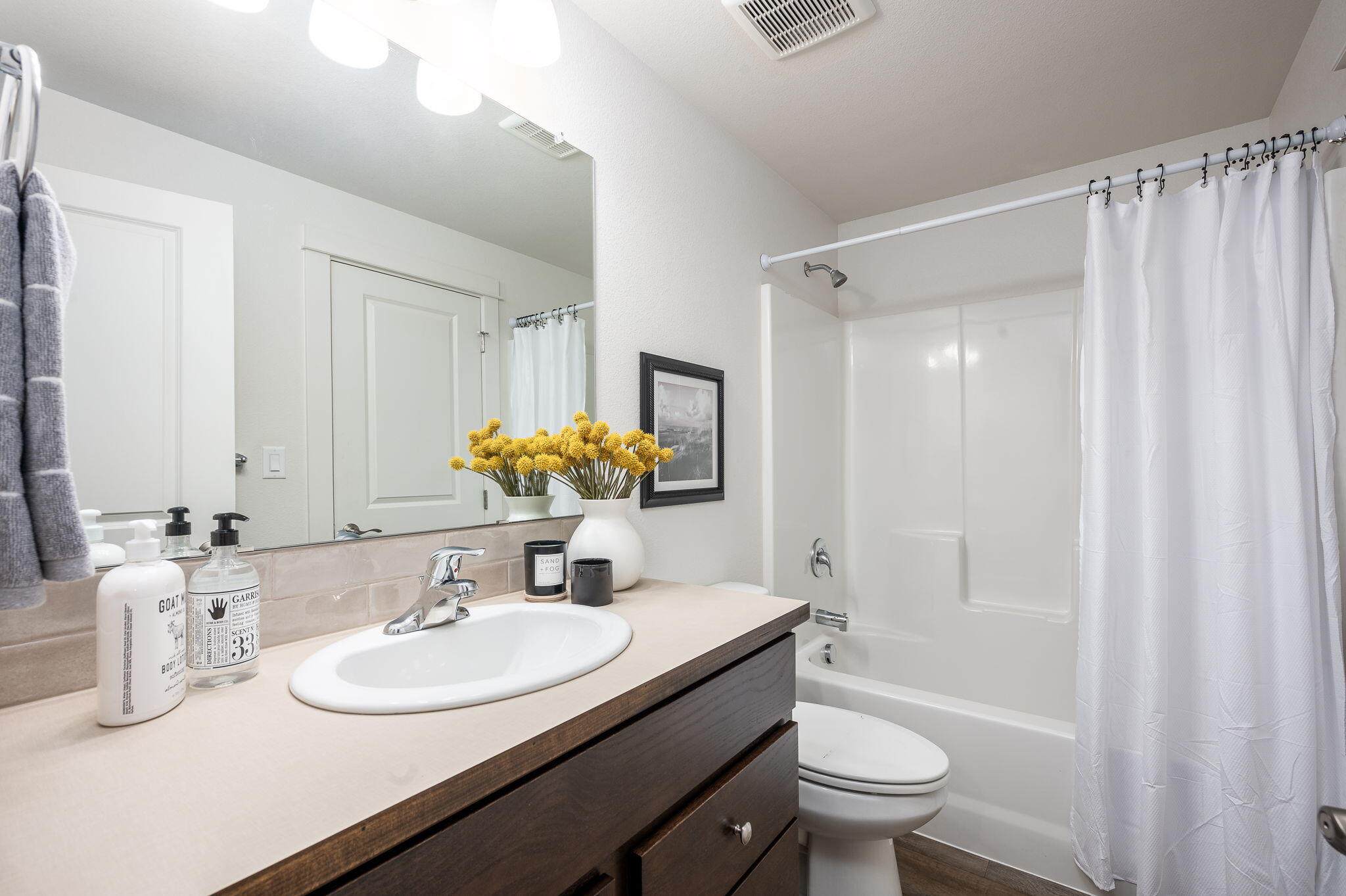 Bathroom with a dark wood vanity, oval sink, and white tub-shower behind a curtain.