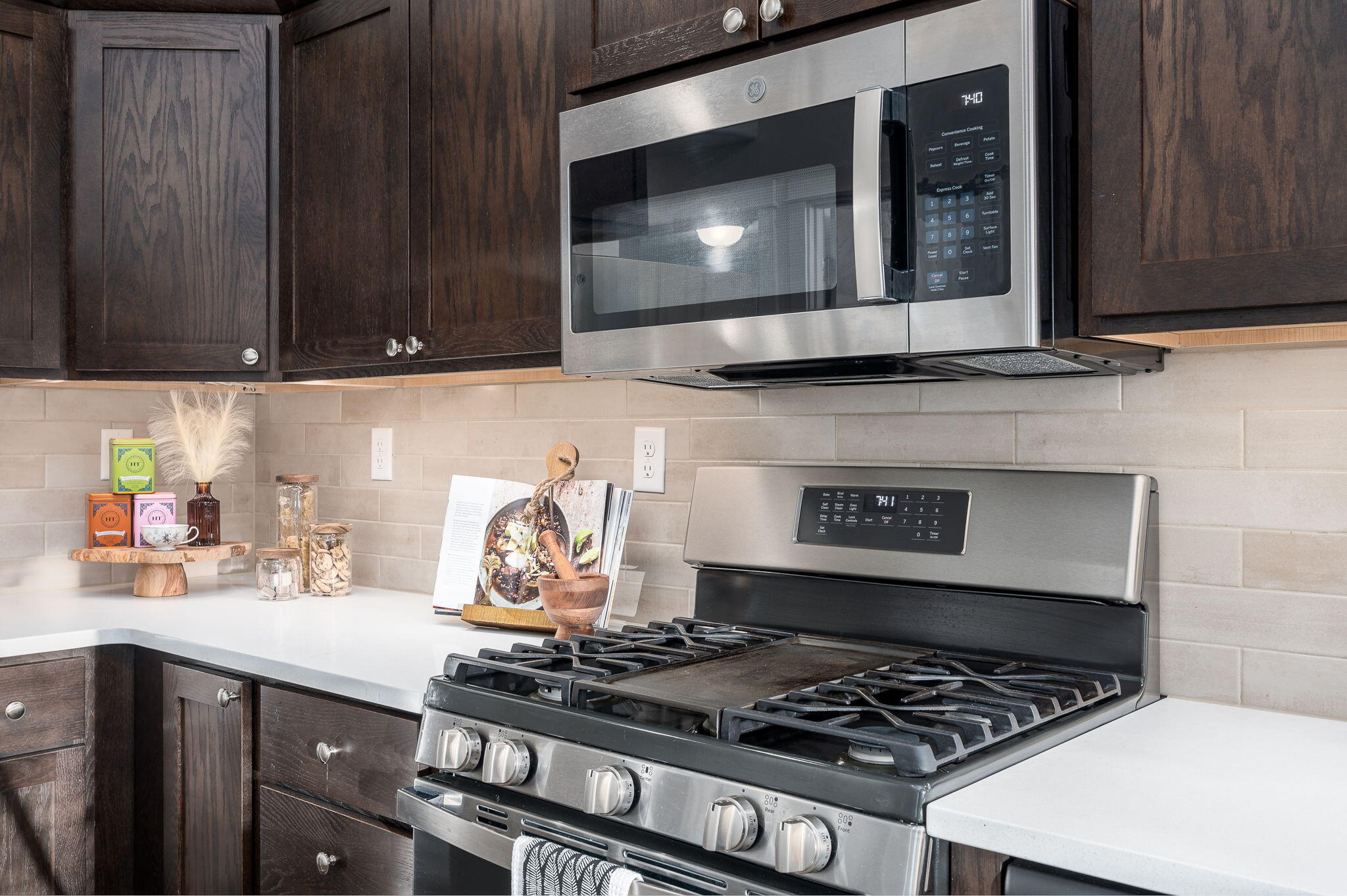 Kitchen with dark wood cabinets, white counters, and a stainless steel gas range beneath a microwave.