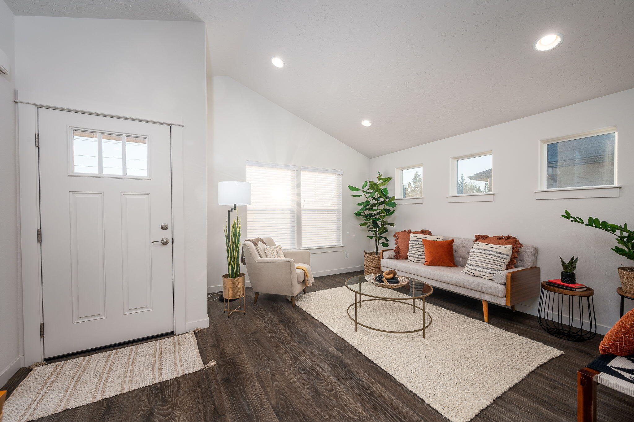 Staged living room with a high sloped ceiling, gray sofa, cream rug, and white front door.