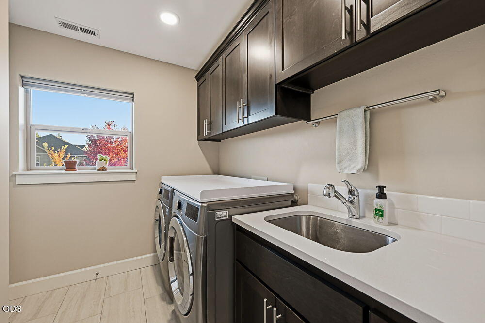 Laundry room with front-loading washer and dryer, a utility sink, dark cabinets, and a window.