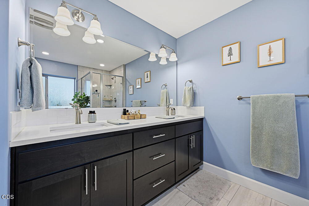 Bathroom with a dark double vanity, two sinks, and a large mirror reflecting the glass shower.